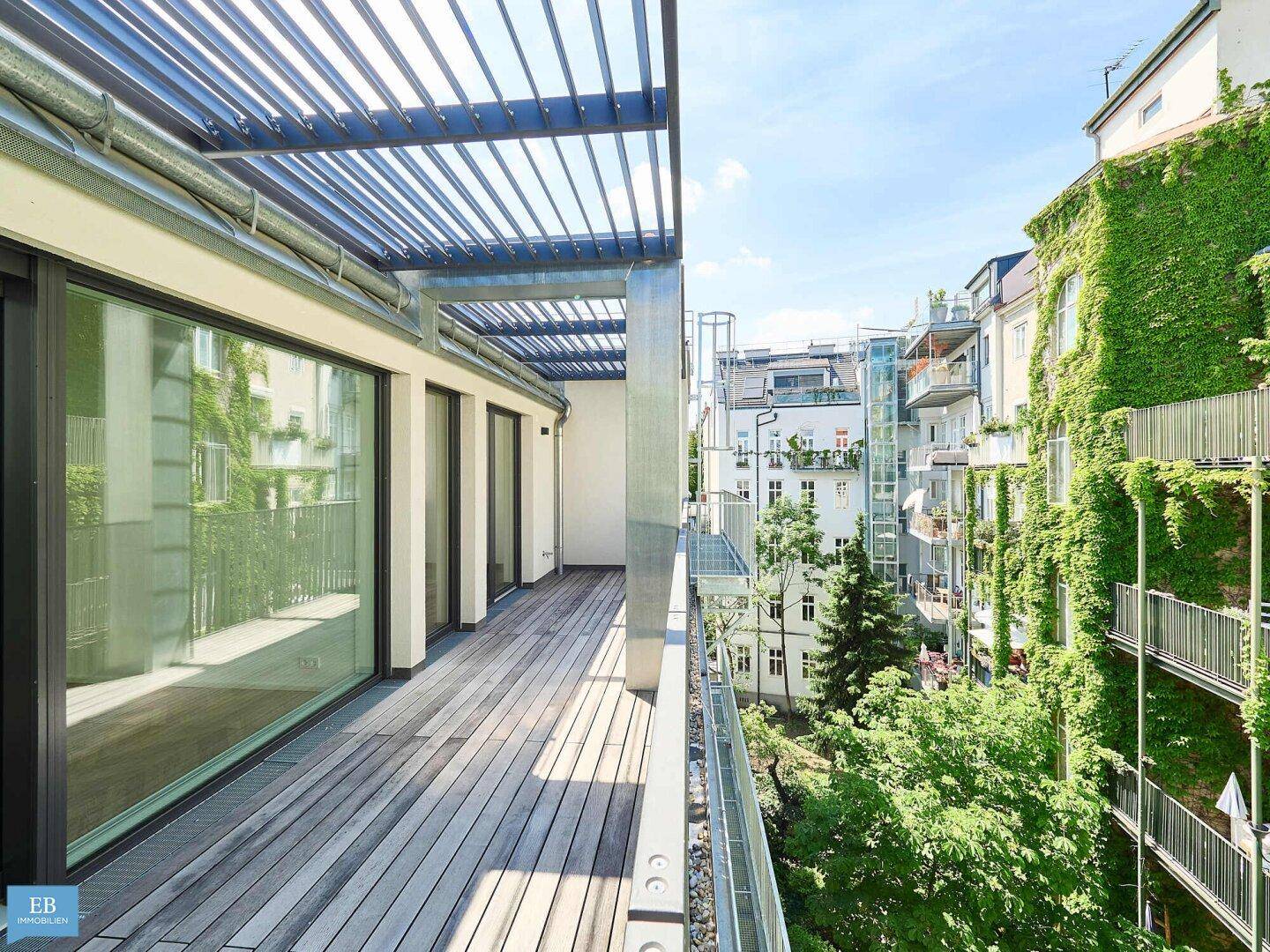 Weitläufige Holzterrasse mit offener Pergola und Ausblick auf die Nachbarschaft und grüne Bäume.