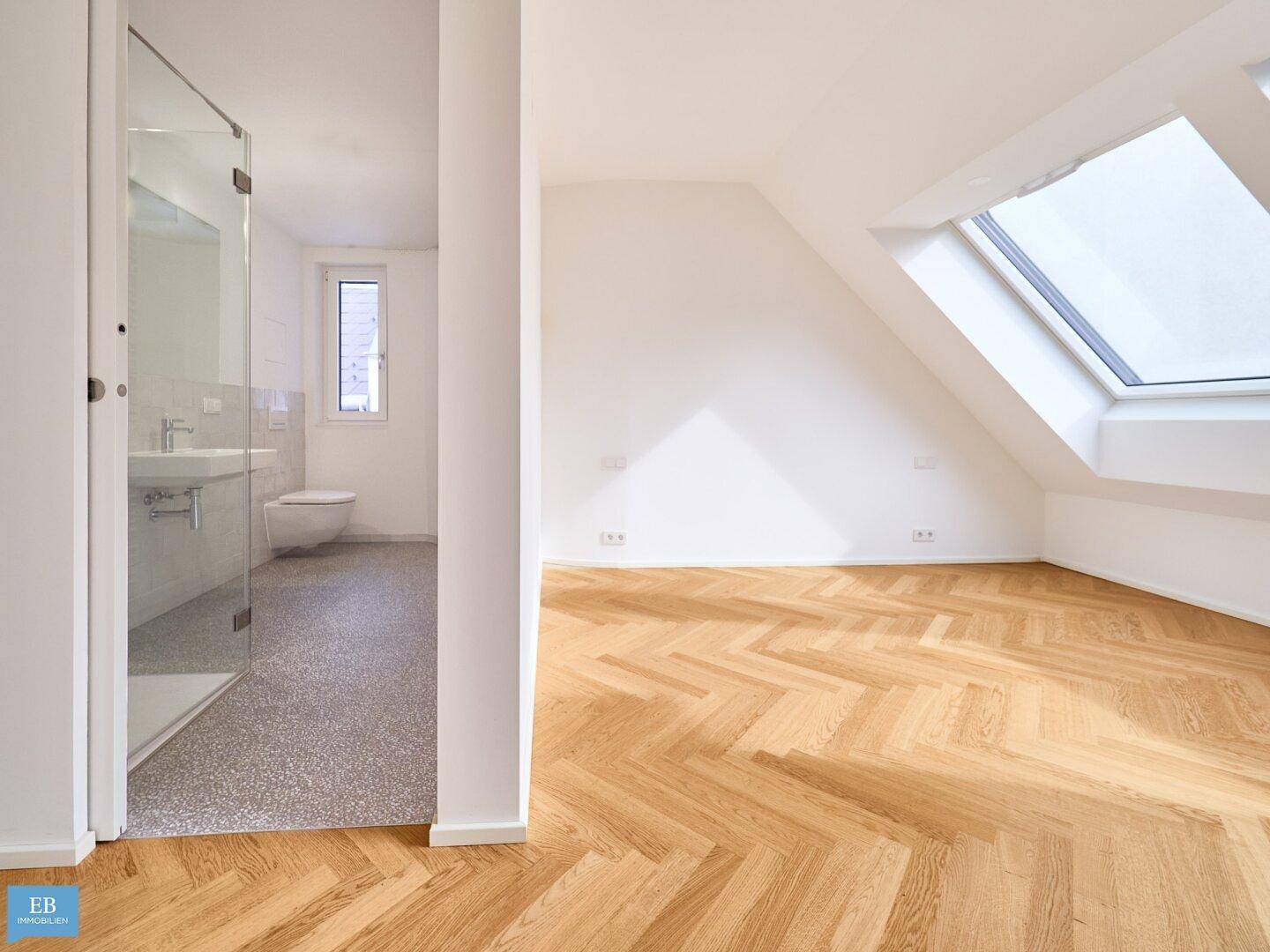 Helles Schlafzimmer mit Fischgrätparkett und Dachfenster, angrenzend an ein modernes Badezimmer.