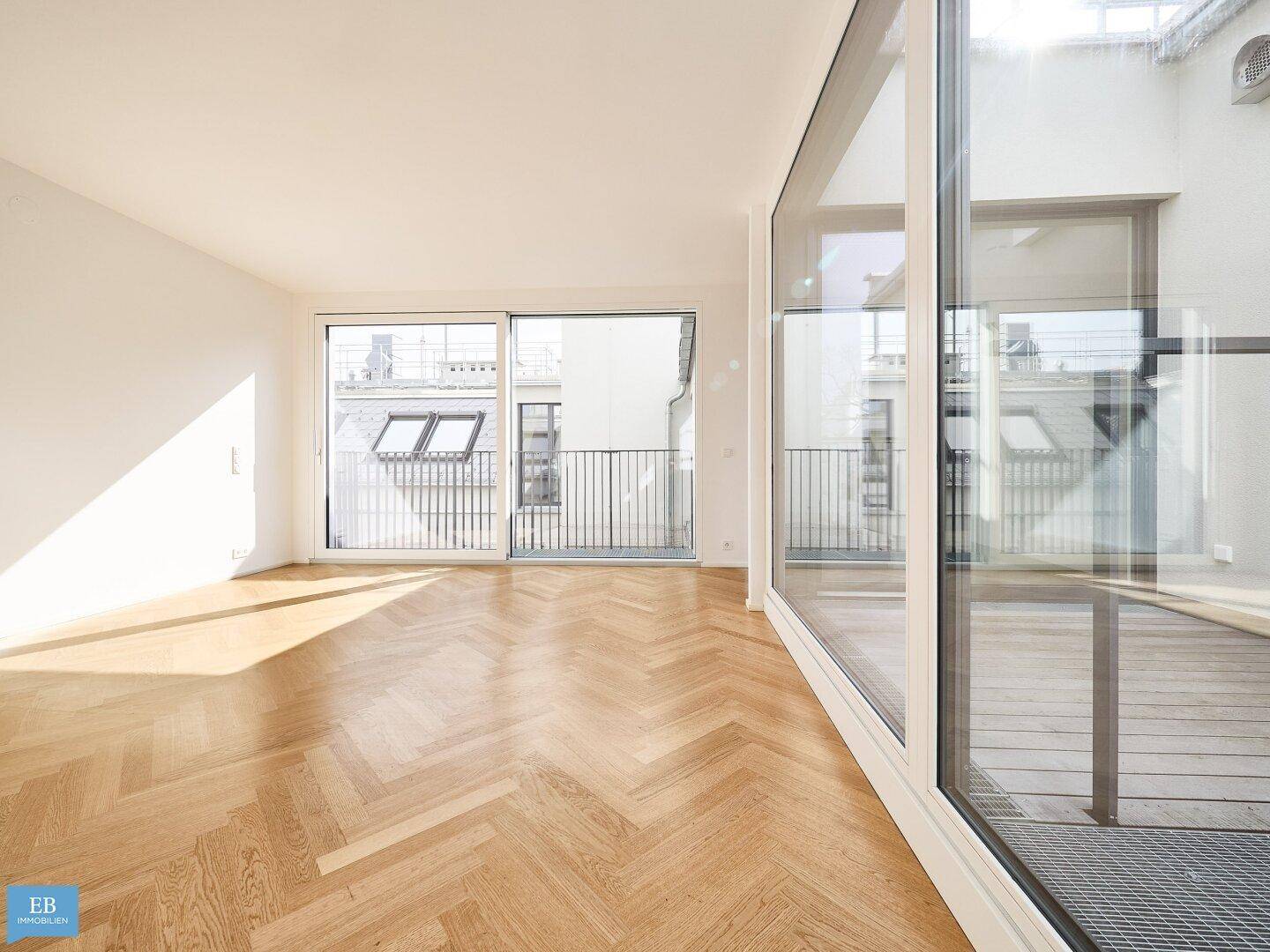 Heller Wohnraum mit Fischgrätparkett und großen Fensterfronten, die viel Tageslicht hereinlassen.