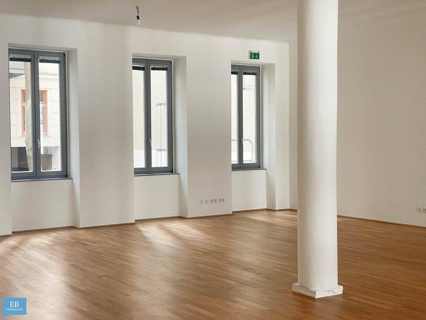 Lichtdurchfluteter Wohnbereich mit Parkettboden und hohen Fenstern, ideal für modernes Wohnen.