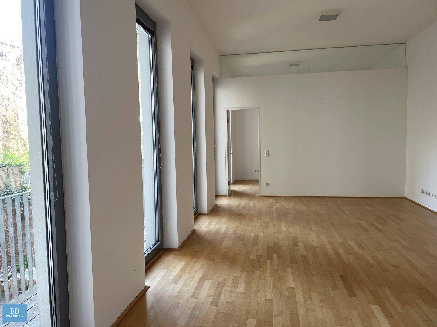 Lichtdurchfluteter Raum mit Zugang zu einem Balkon und Parkettboden, ideal für offenes Wohnen.