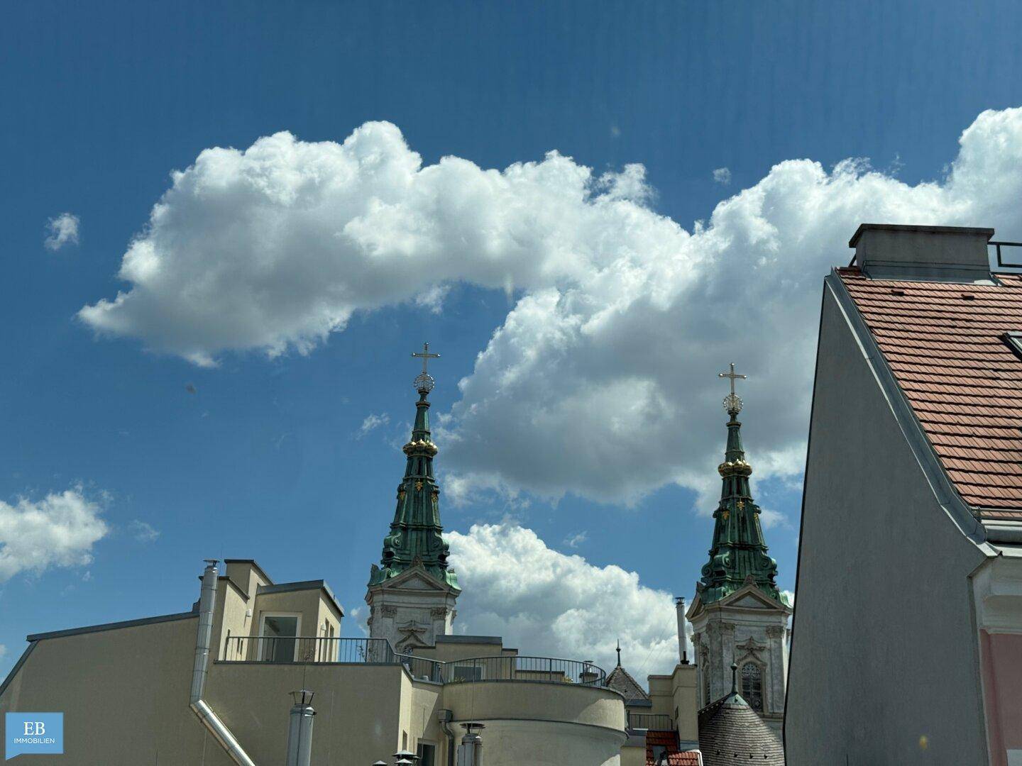Panoramablick auf historische Kirchtürme über den Dächern der Stadt unter einem strahlend blauen Himmel.