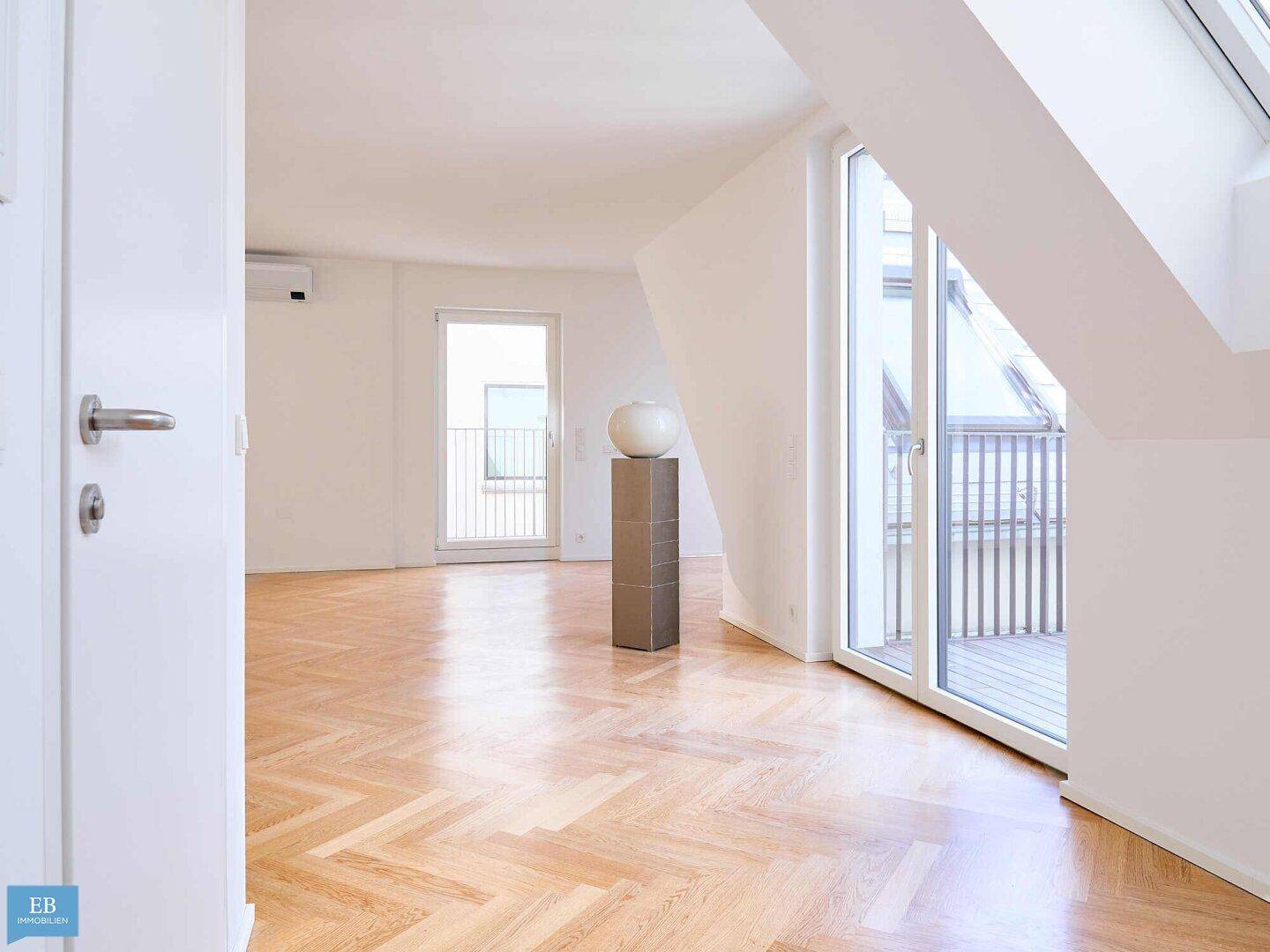 Heller Wohnbereich mit glänzendem Fischgrätparkett, schrägen Wänden und direktem Zugang zu einem Balkon.