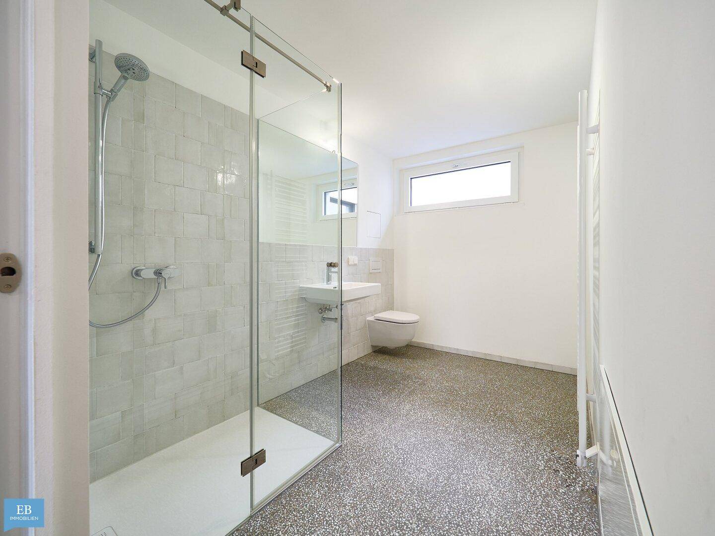 Modernes Badezimmer mit begehbarer Dusche, wandhängendem WC und Waschbecken sowie einem Fenster für Tageslicht.
