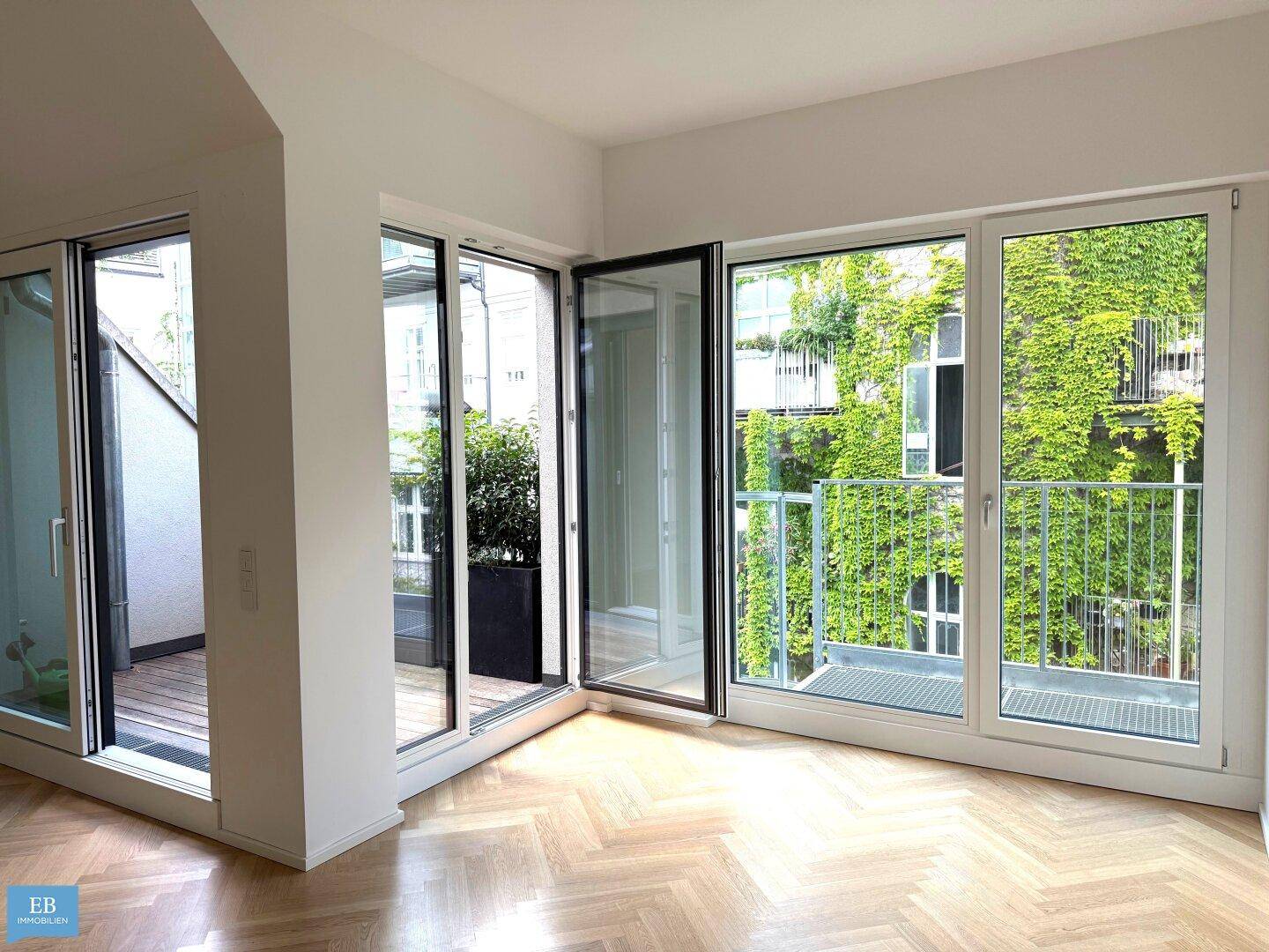 Heller Raum mit Fischgrätparkett und großen Fenstern, die Zugang zu einem Balkon bieten.