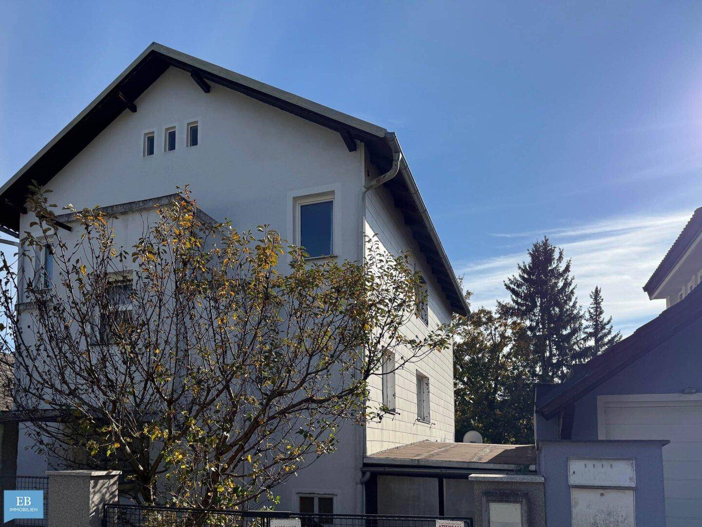 Seitenansicht des Gebäudes mit weißer Fassade und Satteldach unter klarem blauem Himmel.