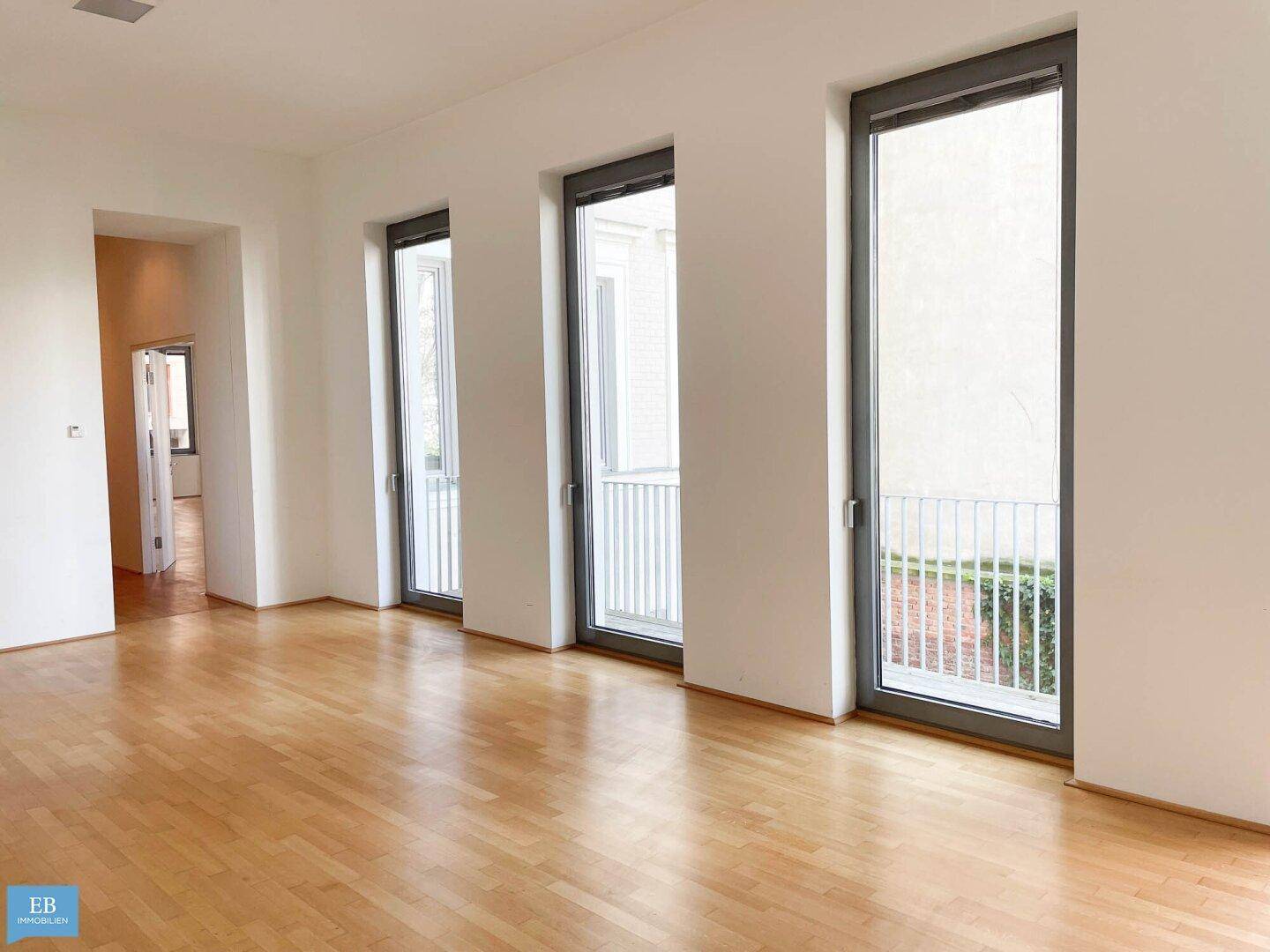 Geräumiger Wohnbereich mit mehreren bodentiefen Fenstern und französischem Balkon.