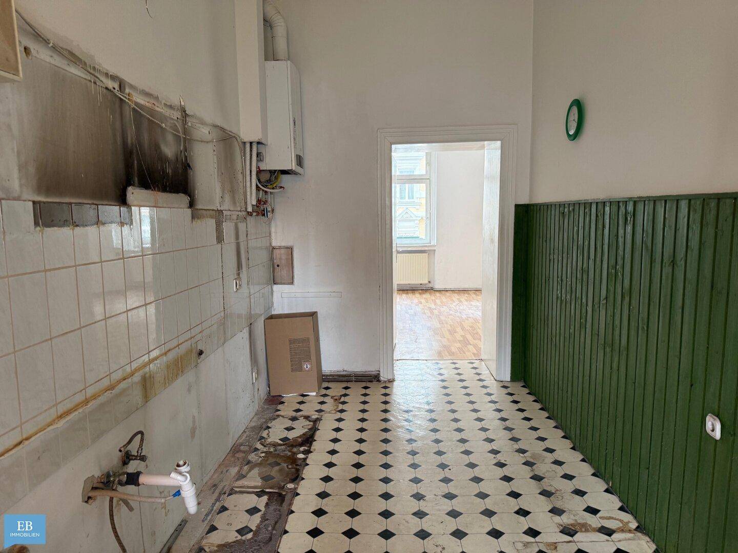 Renovierungsbedürftige Küche mit alten Fliesen, grüner Holzverkleidung und einem Gasboiler.