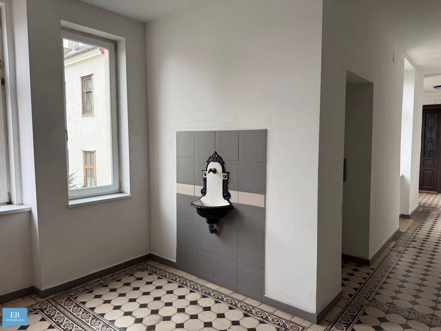 Geräumiger Flur mit gemusterten Bodenfliesen, einem Fenster und einem dekorativen Wandbrunnen.