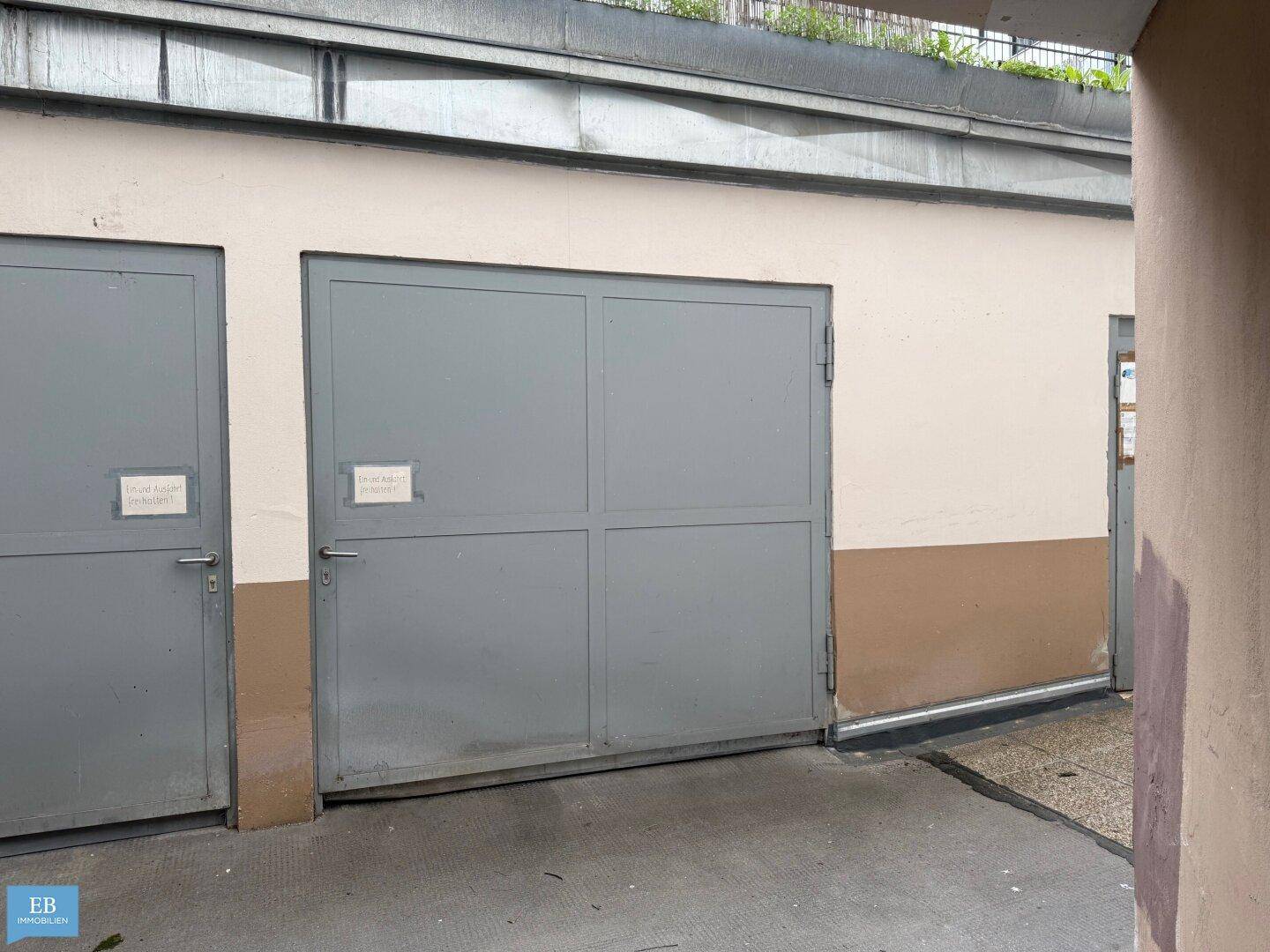 Zwei graue Garagentore an einem Gebäude, die Zugang zu Parkplätzen bieten.