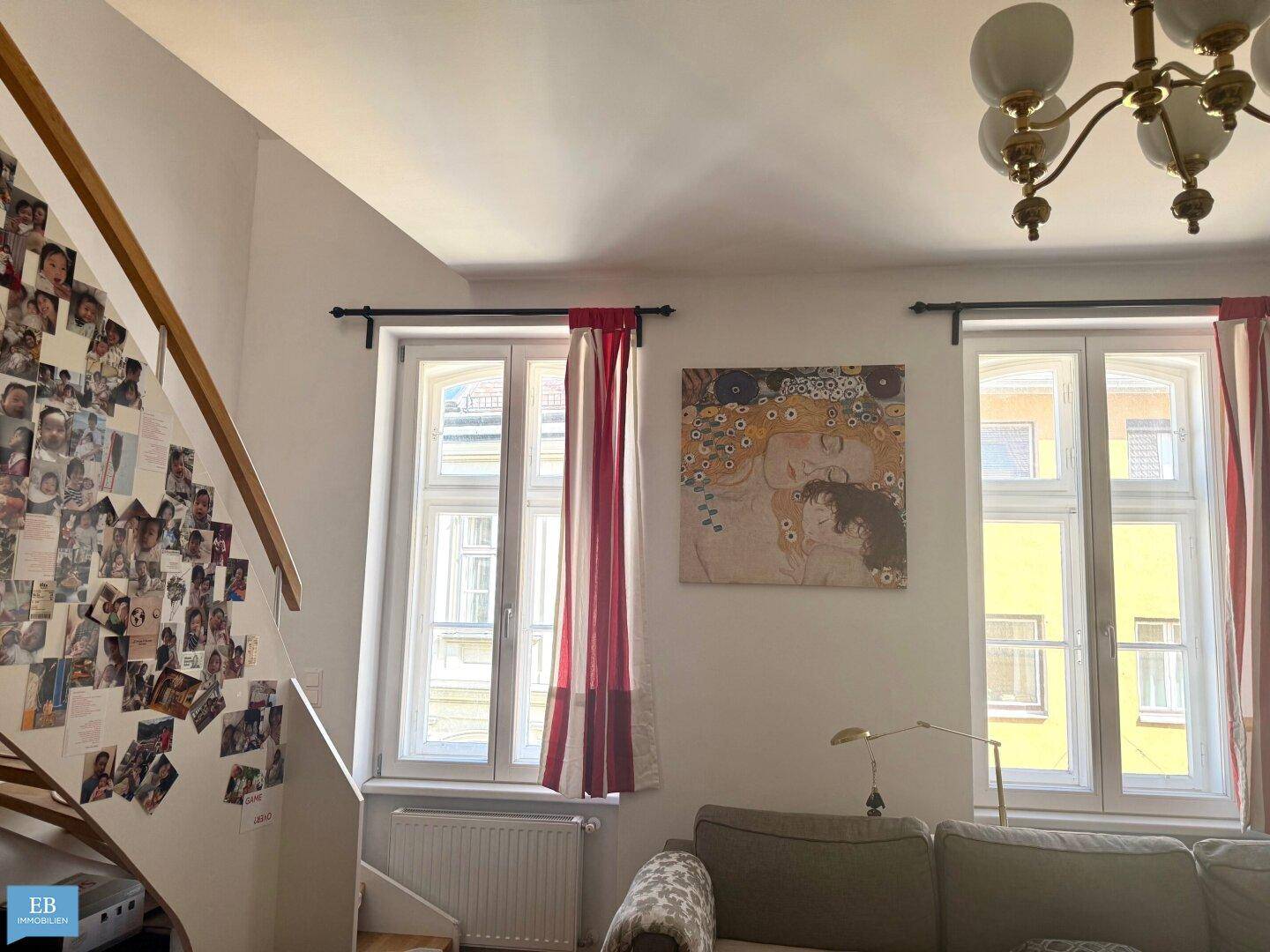 Wohnbereich mit bequemer Couch, großen Fenstern und einer Treppe, die nach oben führt.