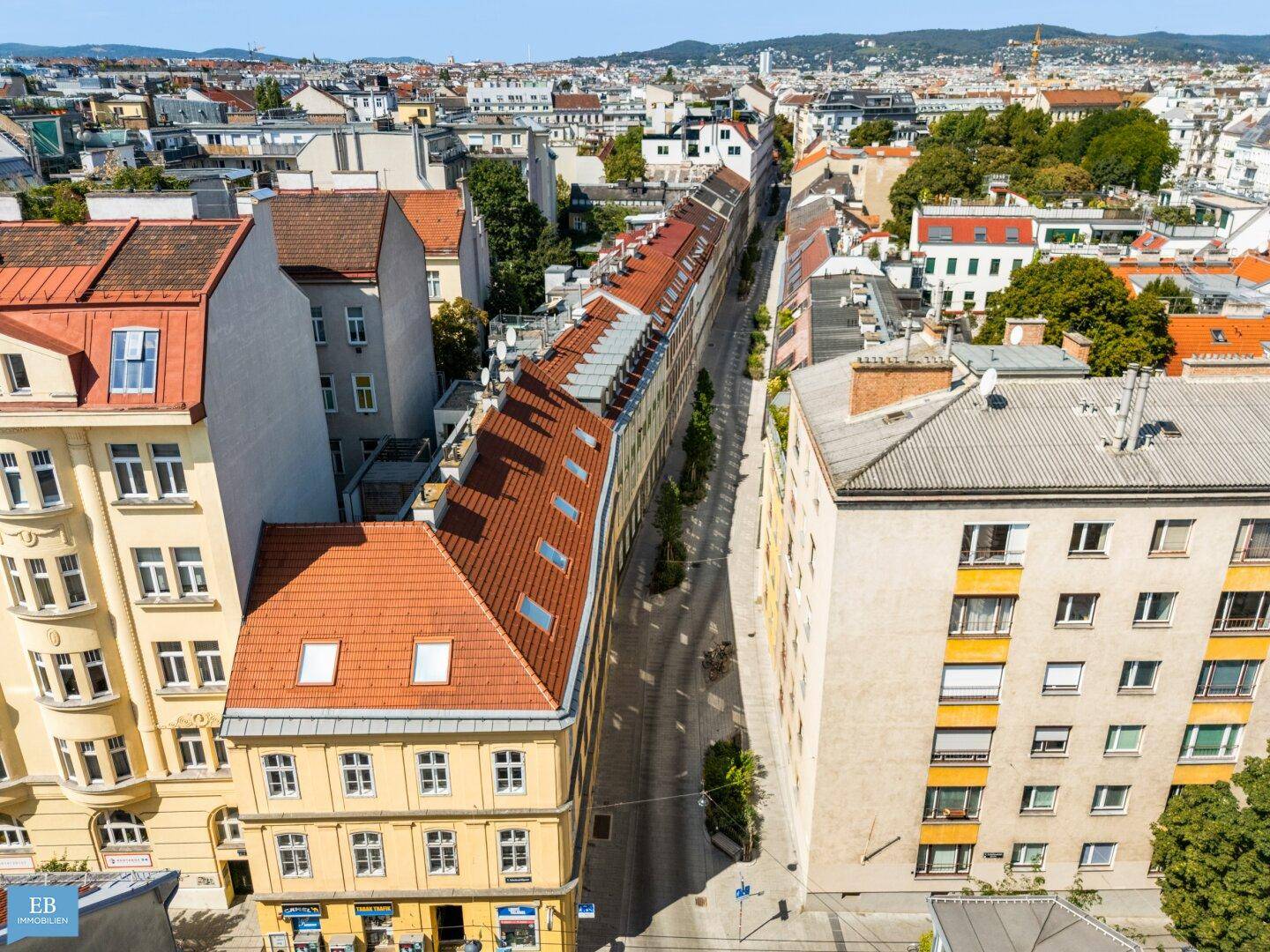 Luftaufnahme einer städtischen Straße mit Gebäuden und Dächern unter blauem Himmel.