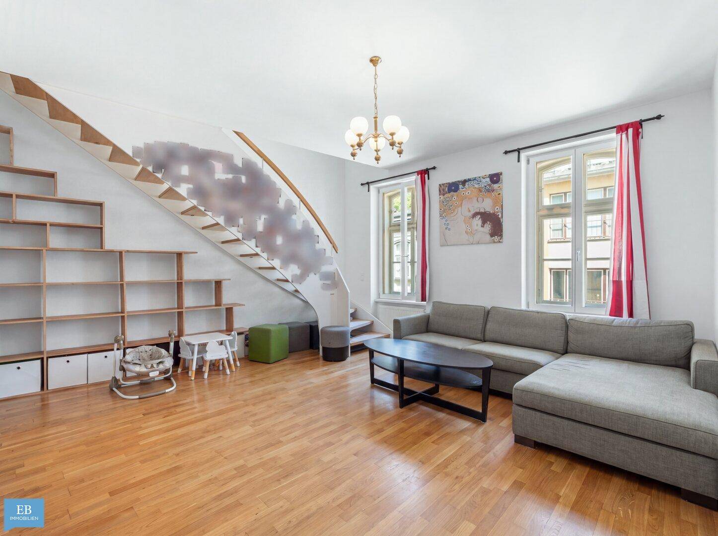 Heller Wohnbereich mit Holzboden, Sofa und integriertem Regal unter der Treppe.