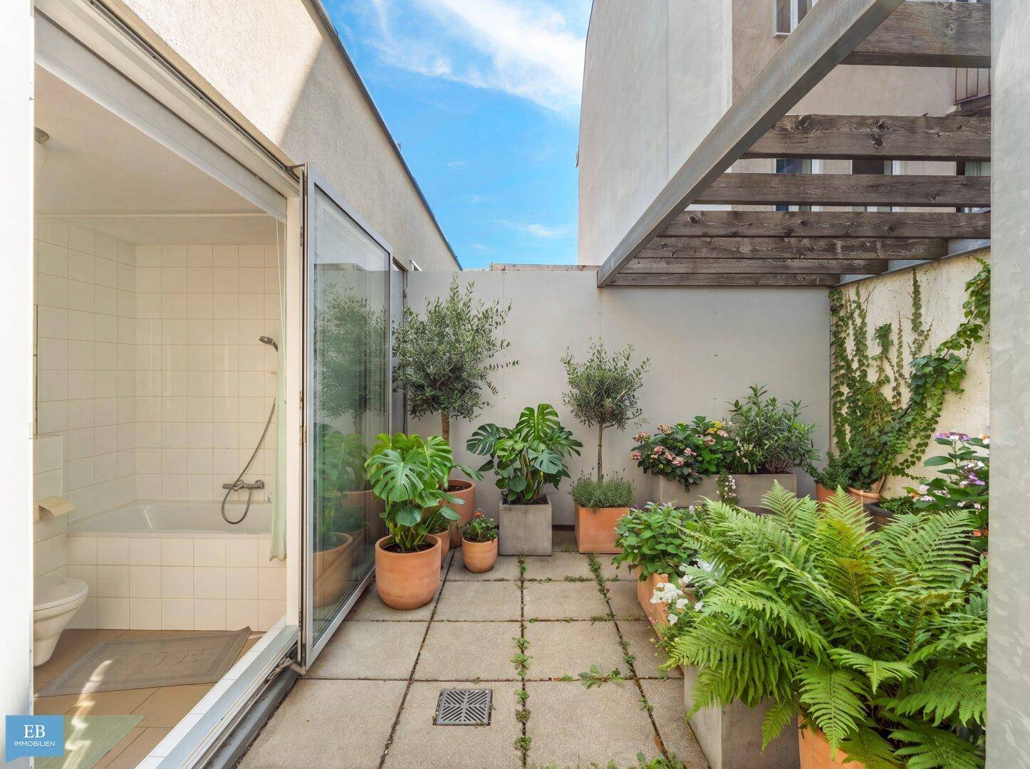 Begrünte Terrasse mit verschiedenen Pflanzen und Blick in ein helles Badezimmer.