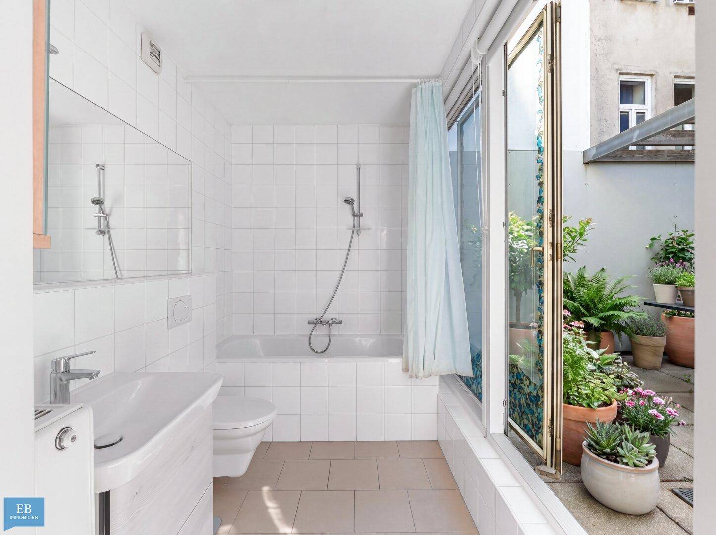 Helles Badezimmer mit Badewanne, weißen Fliesen und Zugang zu einer Außenterrasse.
