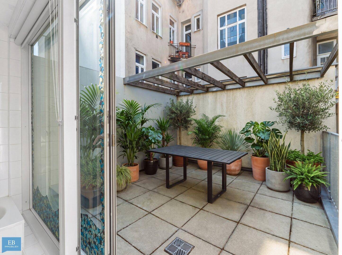 Sonniger Terrassenbereich mit Esstisch, Pflanzen und Zugang zum Badezimmer.