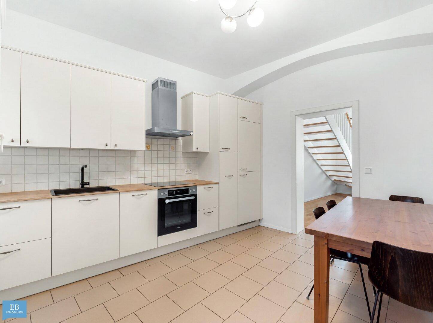 Moderne Einbauküche mit weißen Schränken, Fliesenboden und Esstisch.