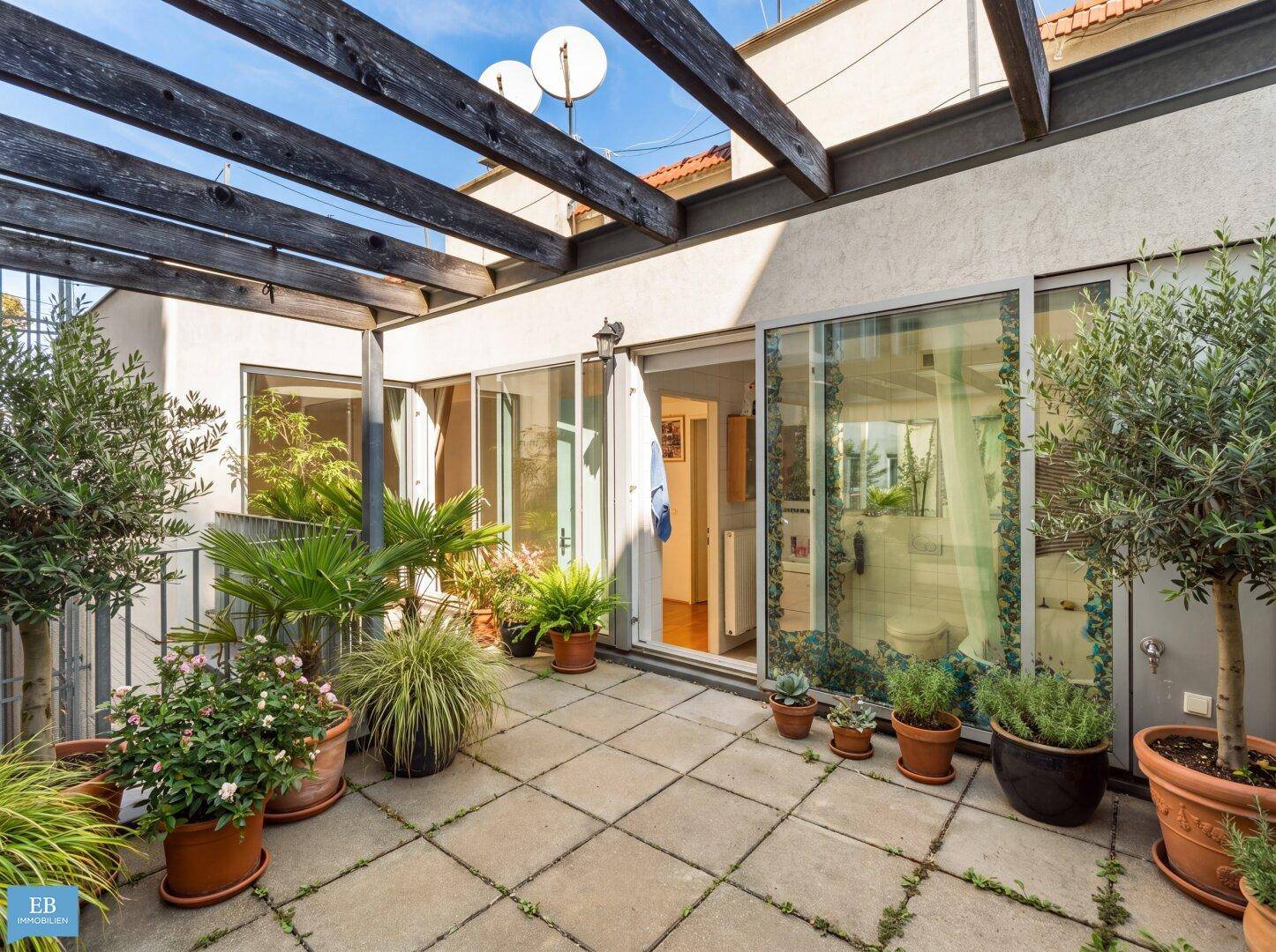 Geräumige Terrasse mit Pflanzen, Pergola und großen Glasschiebetüren zum Innenbereich.
