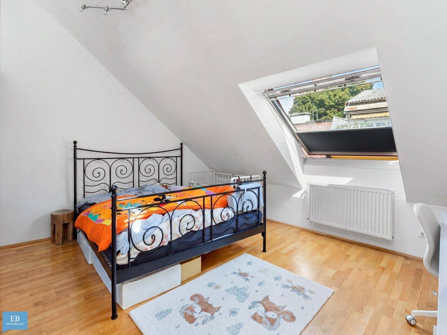 Schlafzimmer im Dachgeschoss mit schräger Decke, Holzboden und großem Dachfenster.