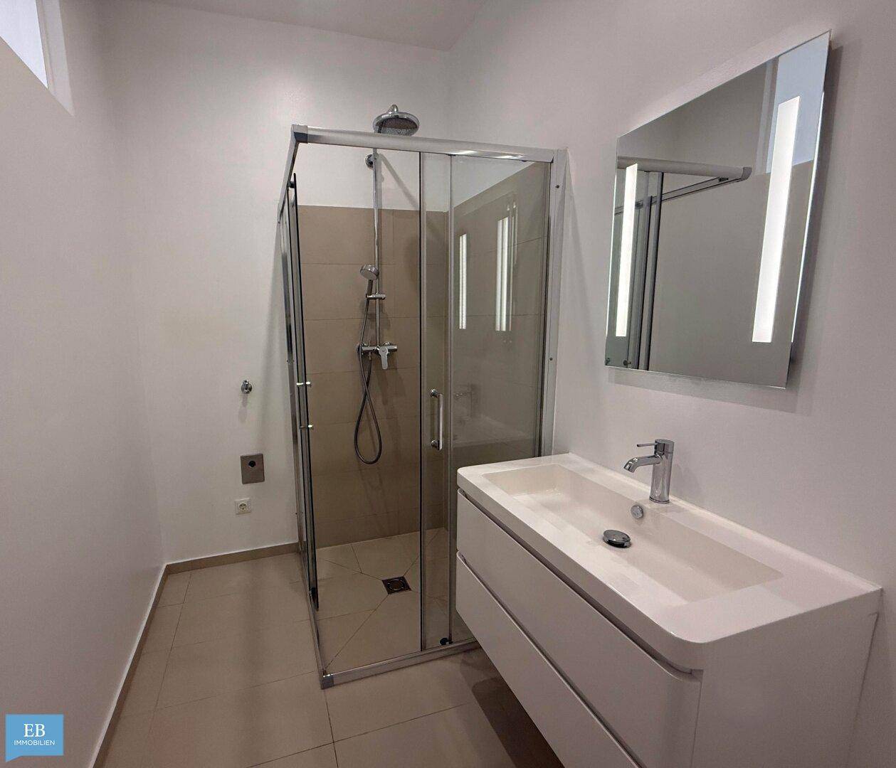 Modernes Badezimmer mit Duschkabine, elegantem Waschtisch und beleuchtetem Spiegel.