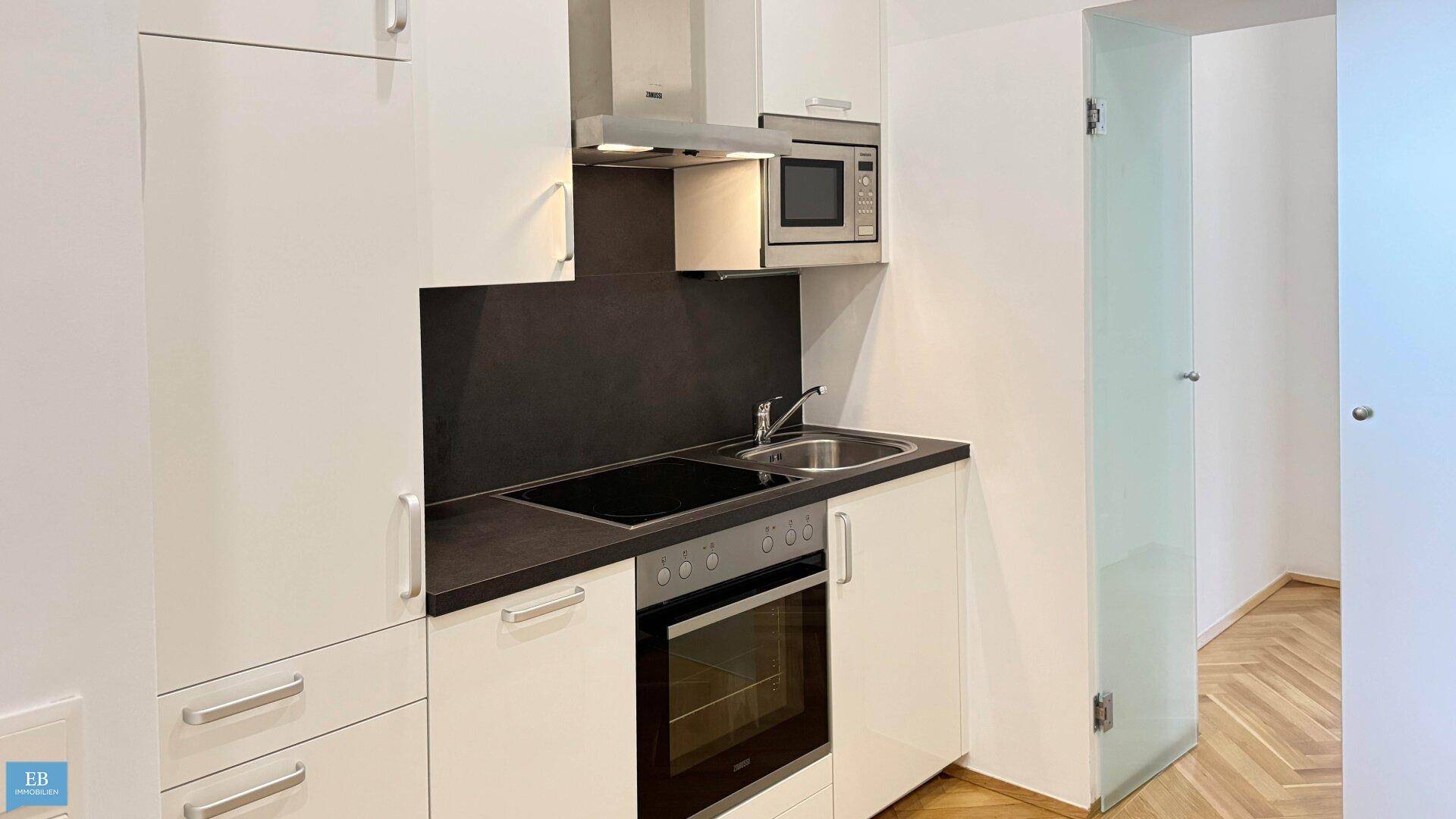 Moderne Küchenzeile mit weißen Schränken, integriertem Backofen und Mikrowelle sowie einer Glastür.