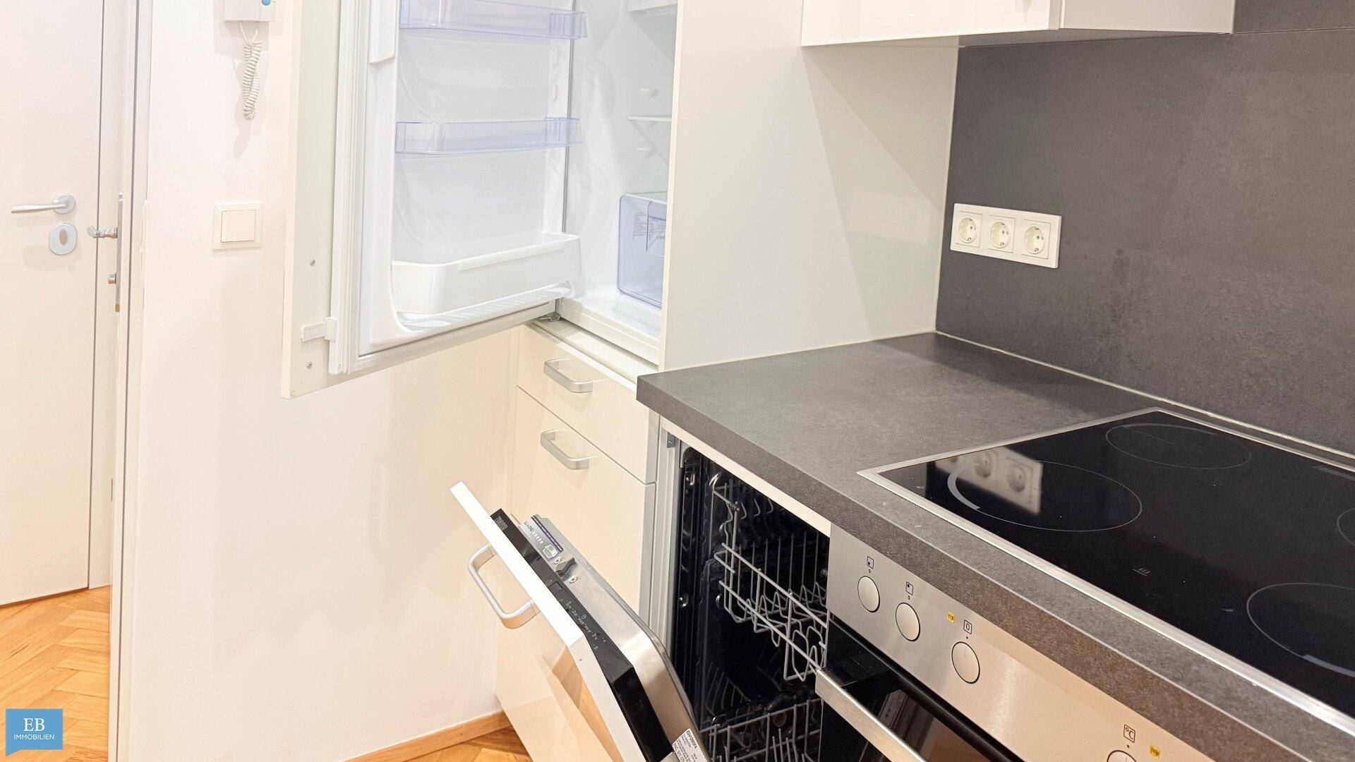 Detailansicht der Küche mit geöffnetem Geschirrspüler und Kühlschrank, zeigt moderne Einbaugeräte.