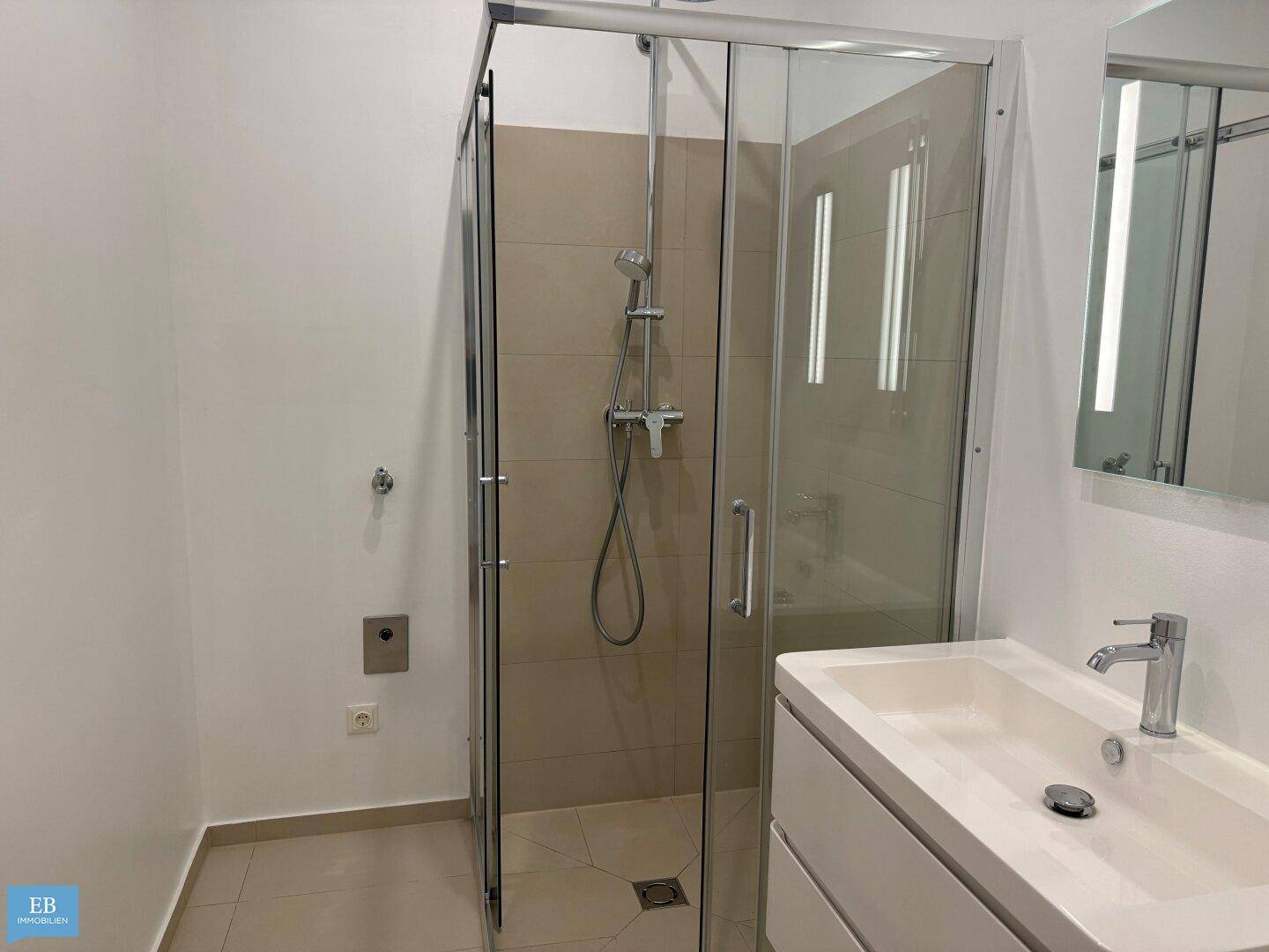 Duschbereich im modernen Badezimmer mit Glasabtrennung und beigefarbenen Fliesen.