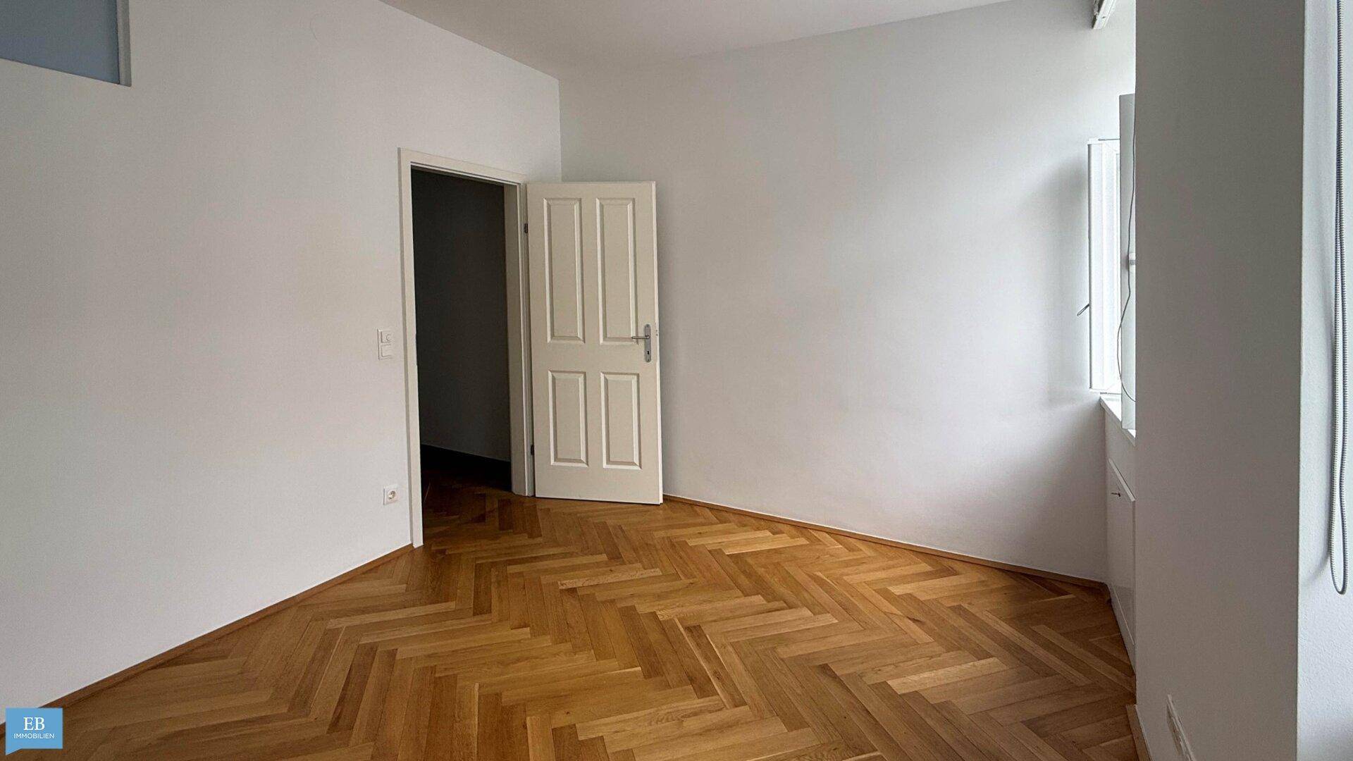 Leerer Raum mit elegantem Fischgrätparkett und einer weißen Tür, bereit zur Einrichtung.