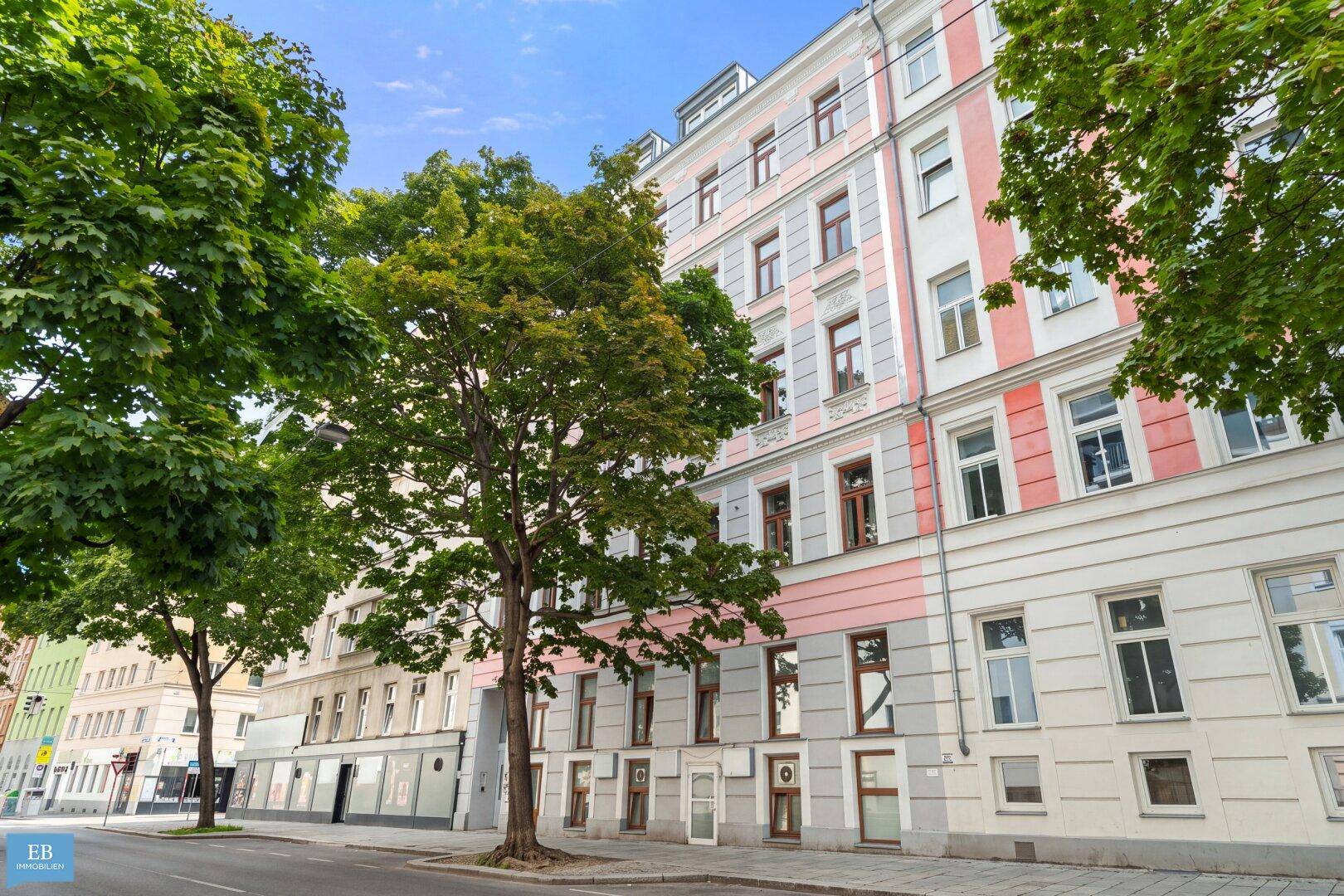 Historisches Gebäude mit klassischer Fassade und Bäumen an einer städtischen Straße.