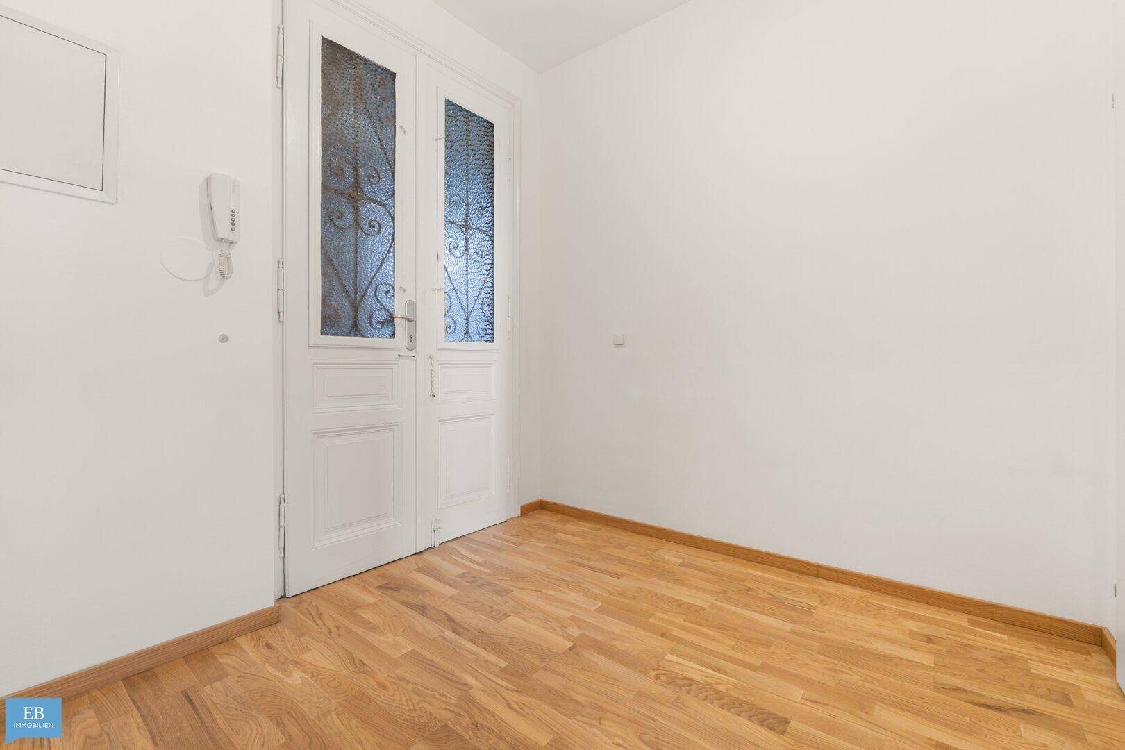 Leeres Zimmer mit Parkettboden und einer Doppeltür mit Glaseinsätzen.