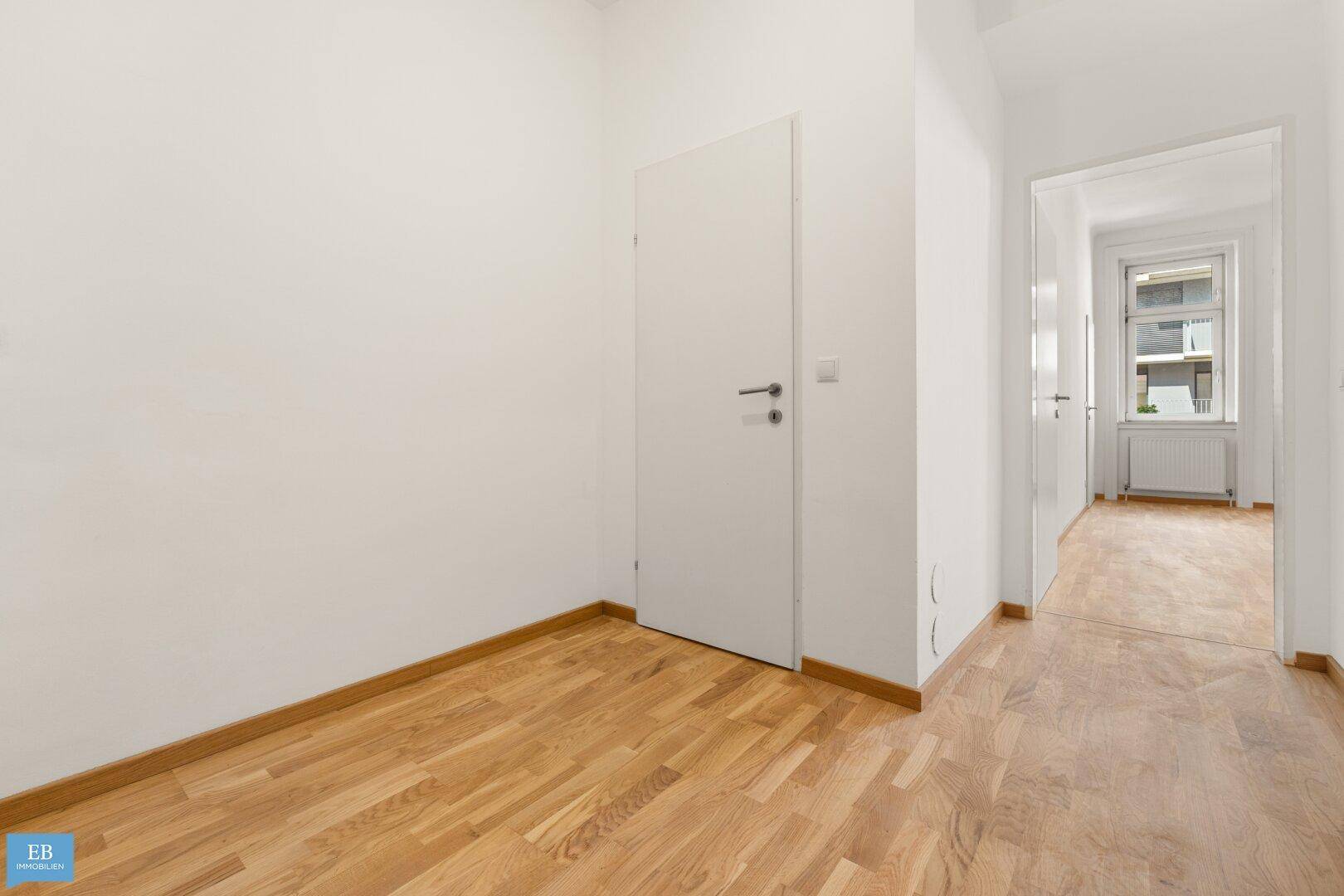 Helles Zimmer mit Parkettboden und Zugang zu einem weiteren Raum.