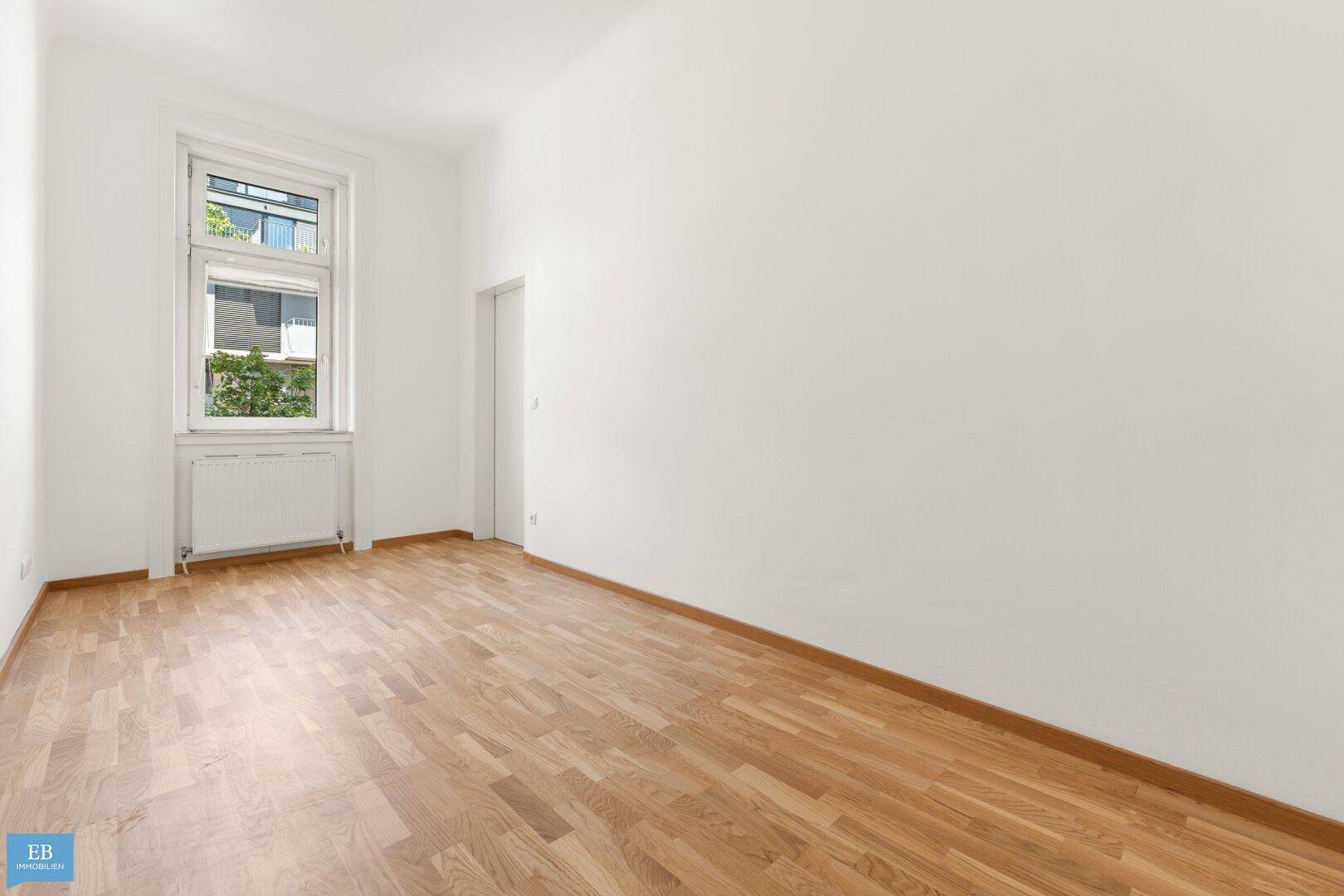 Helles, leeres Zimmer mit Parkettboden und einem Fenster, bereit zur Einrichtung.