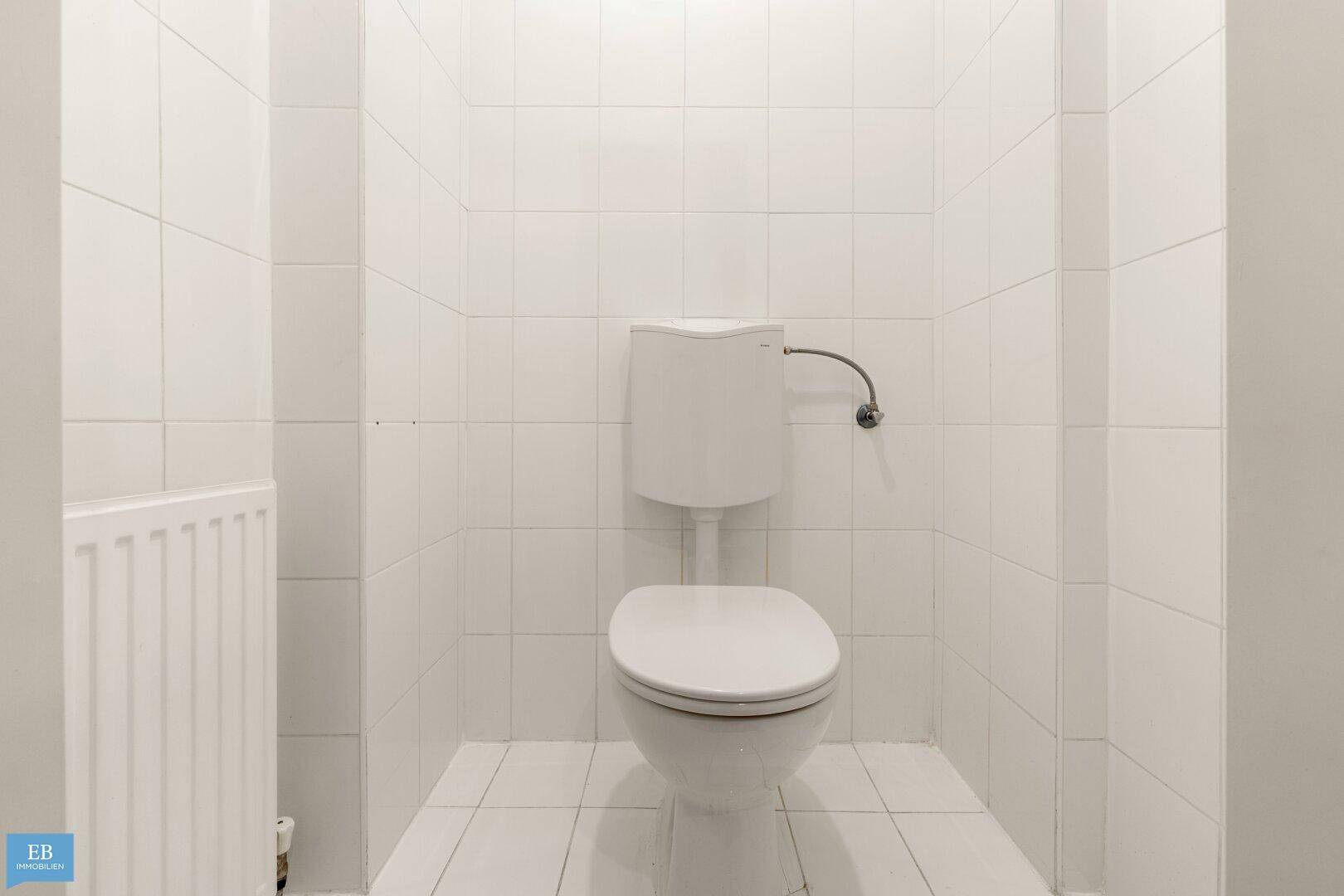 Separates WC mit weißen Fliesen und einem Heizkörper.