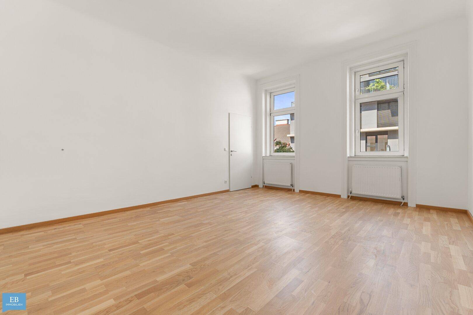 Helles, leeres Zimmer mit Parkettboden und zwei Fenstern, bereit zur Einrichtung.
