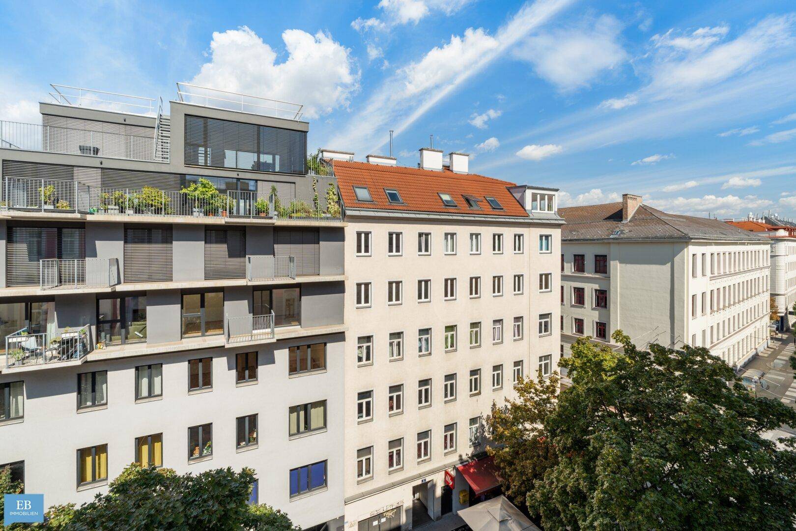 Ansicht mehrerer Gebäude mit modernen Fassaden, Balkonen und Dachterrassen unter blauem Himmel.