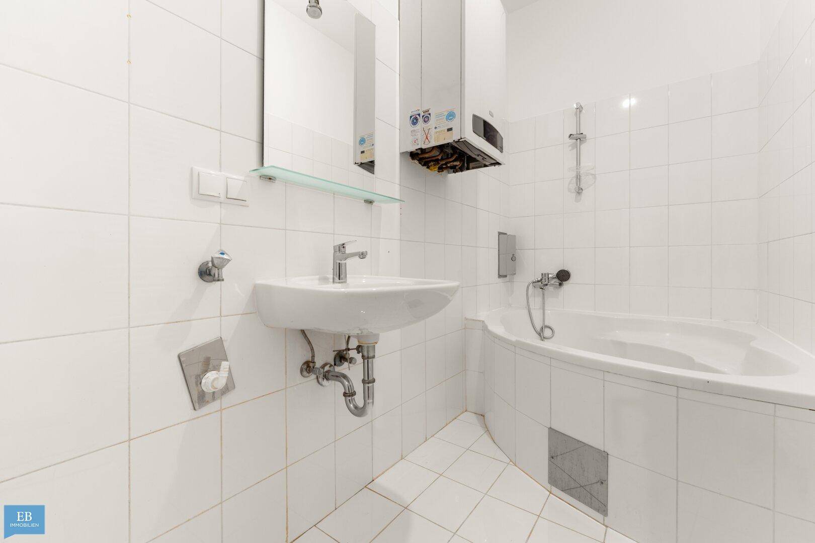 Funktionales Badezimmer mit weißen Fliesen, Badewanne und Waschbecken.