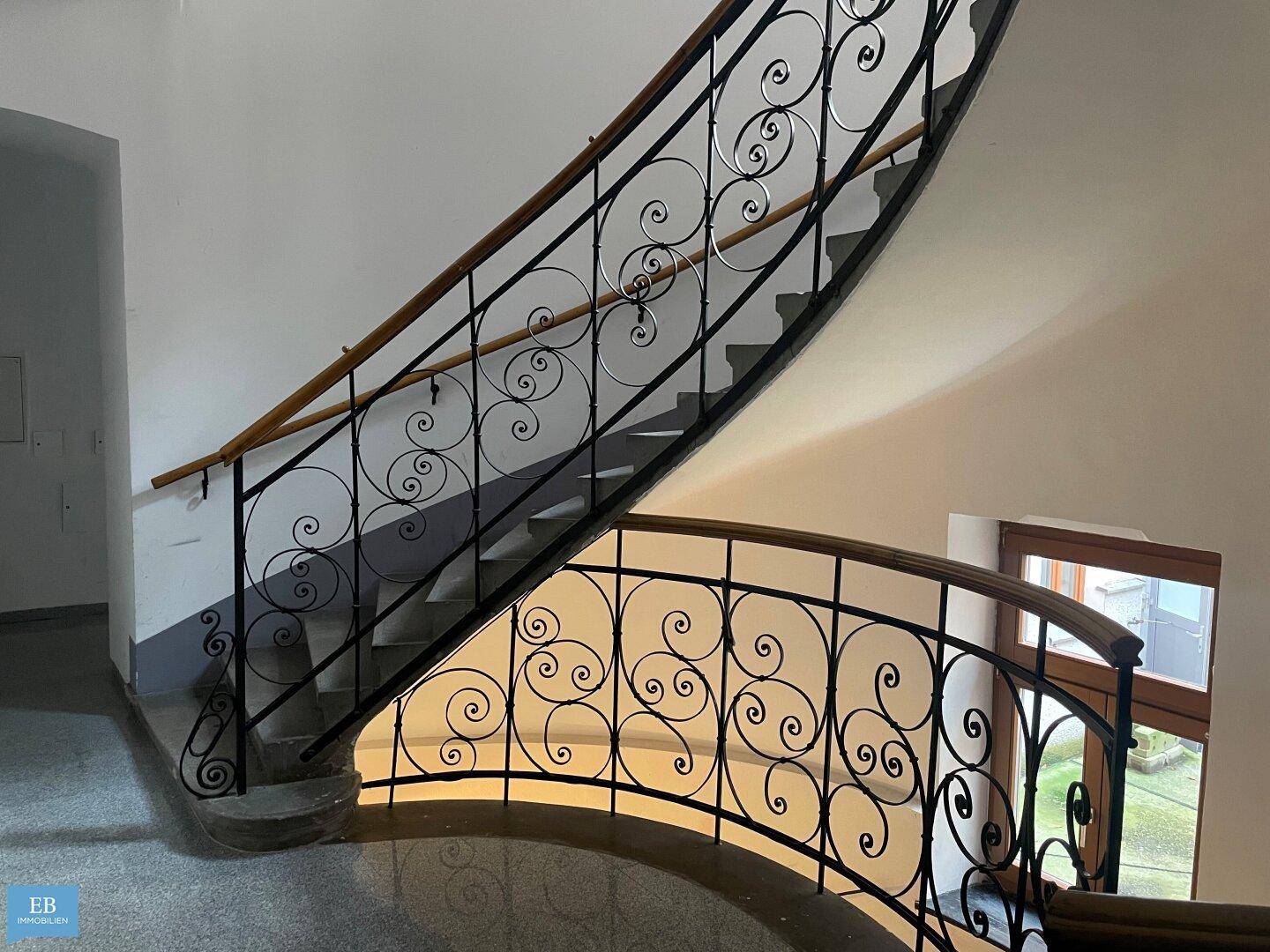 Elegantes Treppenhaus mit schmiedeeisernem Geländer und Holzhandlauf in einem Altbau.