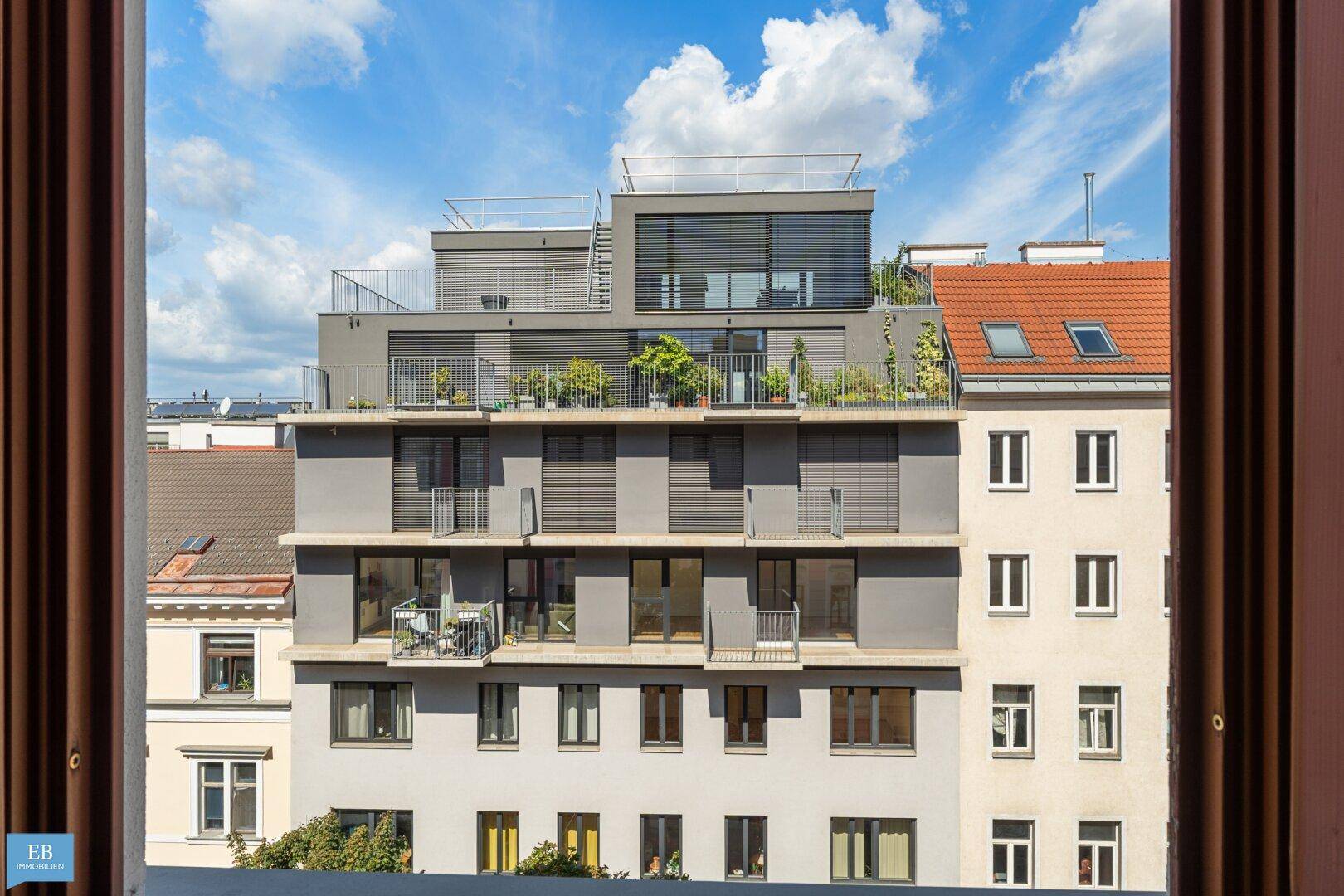 Blick aus einem Fenster auf moderne und klassische Stadtgebäude mit Balkonen und Dachterrassen.
