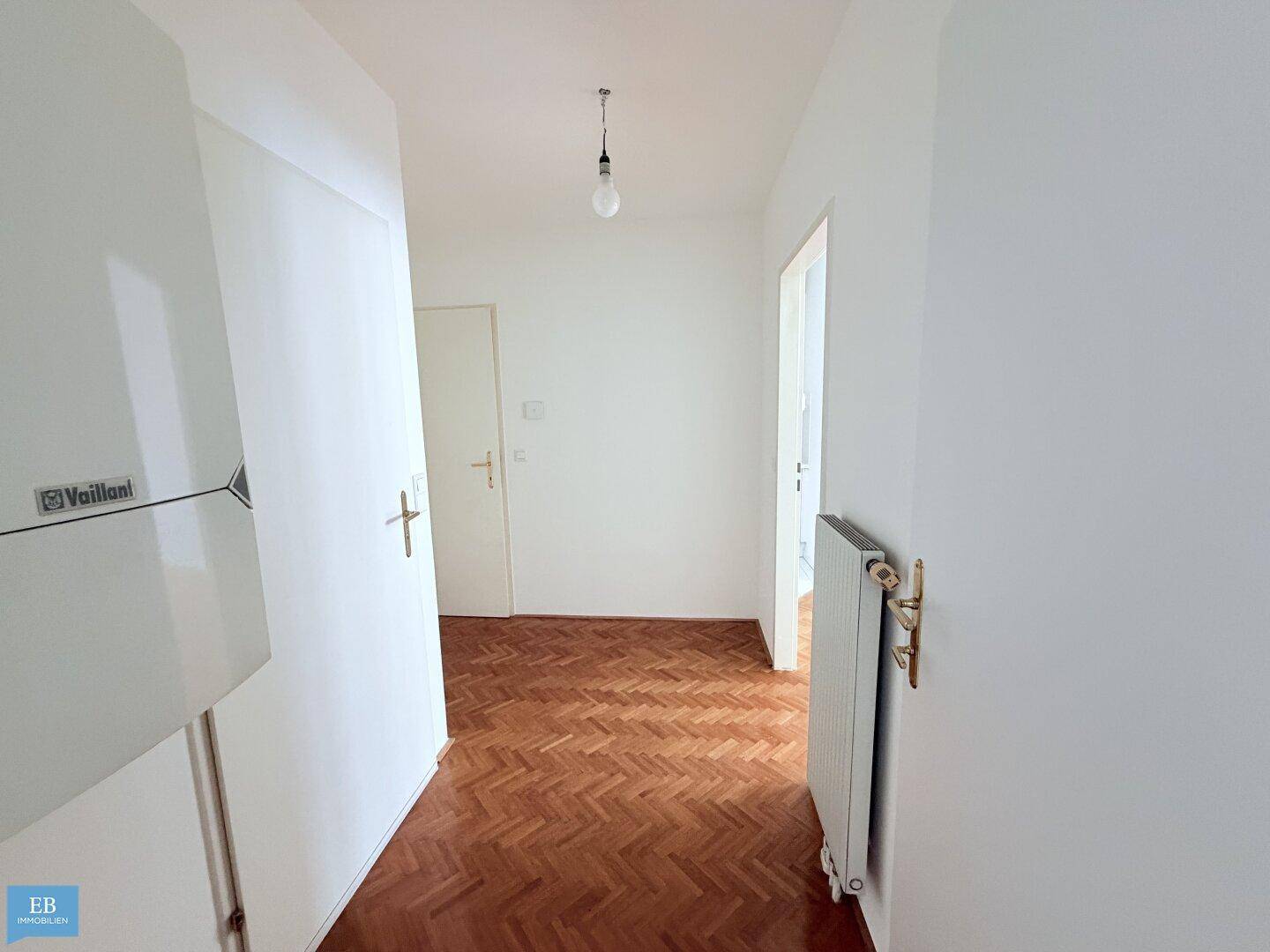 Langer Flur mit Fischgrätparkett und Heizungsanlage an der Wand.