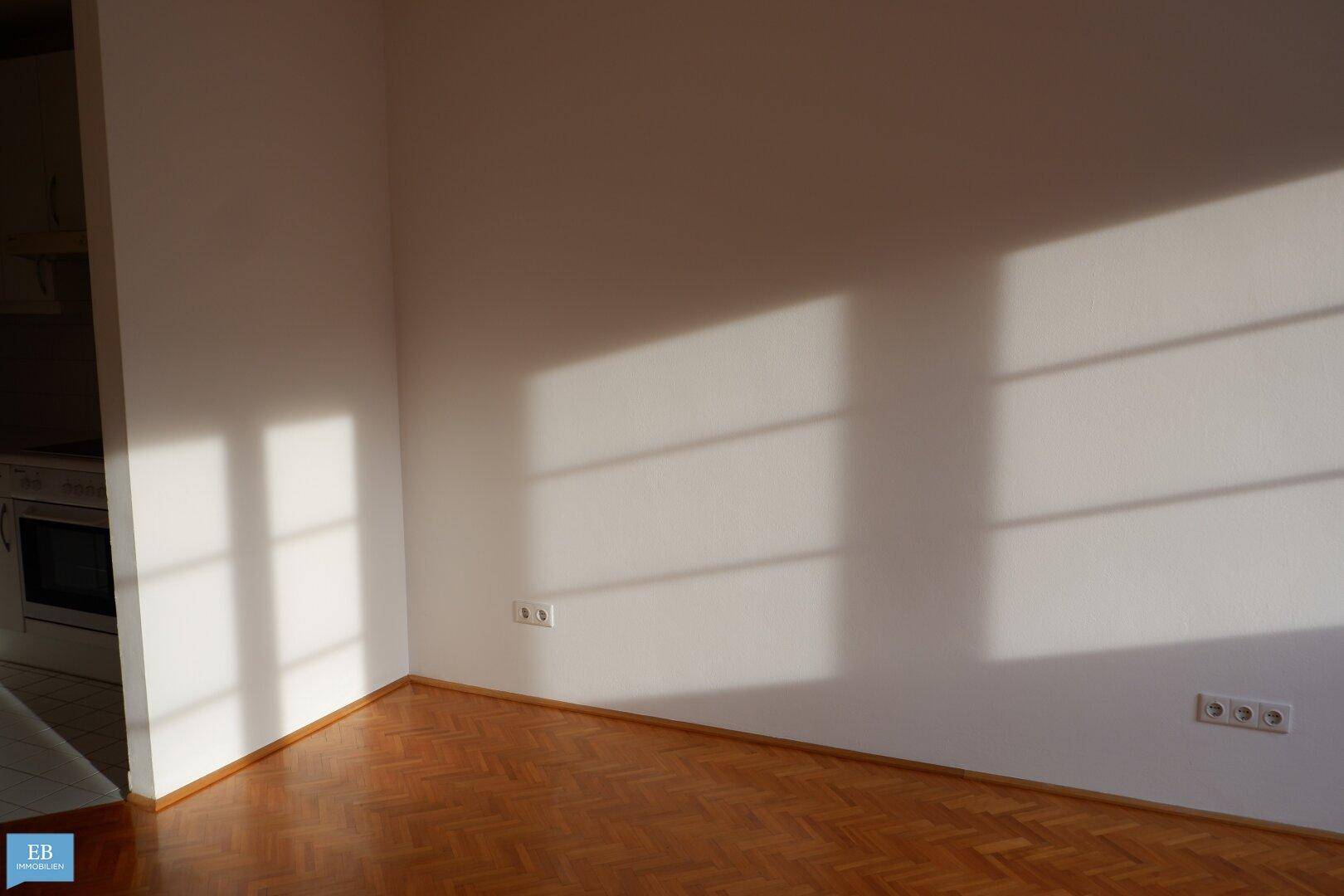 Sonnige Ecke eines Zimmers mit Fischgrätparkett und hellen Wänden, ideal für gemütliche Stunden.