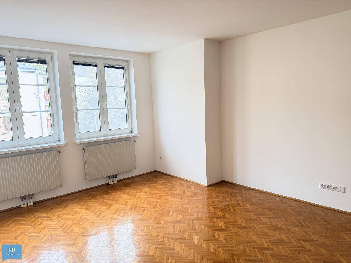 Geräumiges Zimmer mit hellem Fischgrätparkett und weißen Wänden, bereit zur Einrichtung.