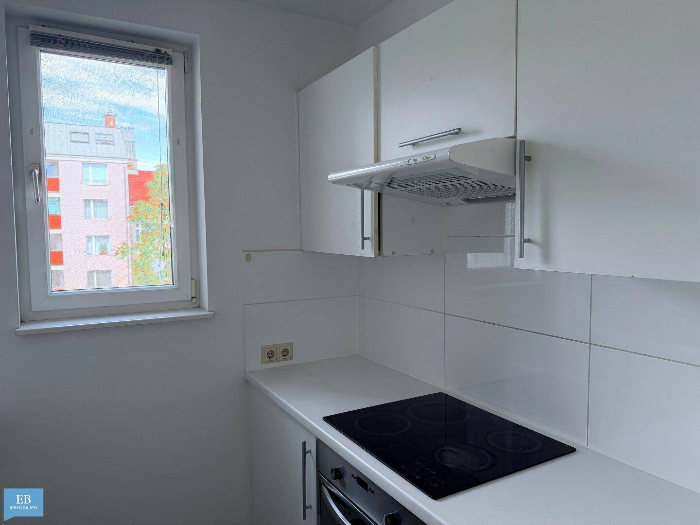 Moderne Küchenzeile mit weißer Arbeitsplatte, Induktionskochfeld und Dunstabzugshaube.