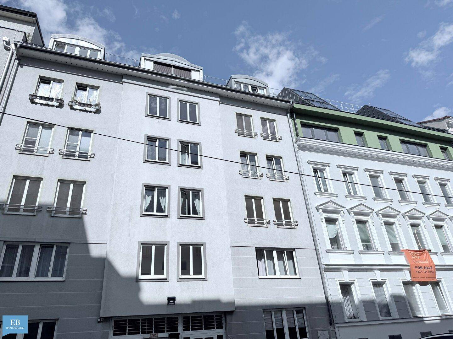 Fassade eines Wohngebäudes mit vielen Fenstern und einem 'For Sale'-Banner.