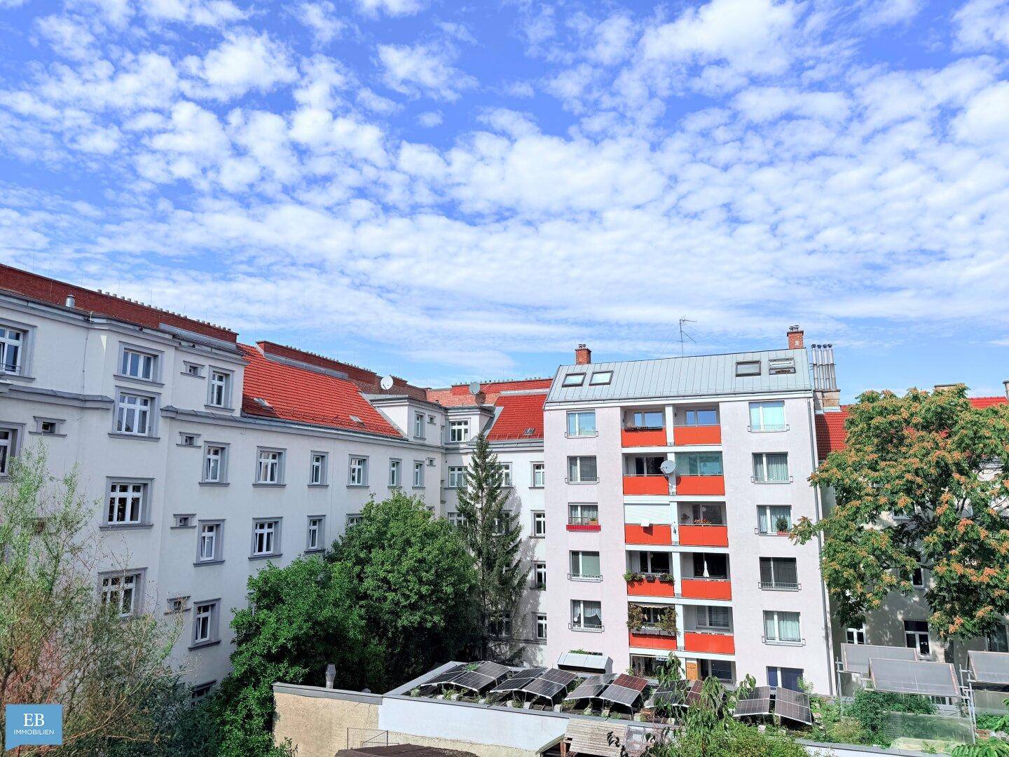 Blick auf mehrere Wohngebäude mit roten Dächern und grünen Bäumen unter blauem Himmel.