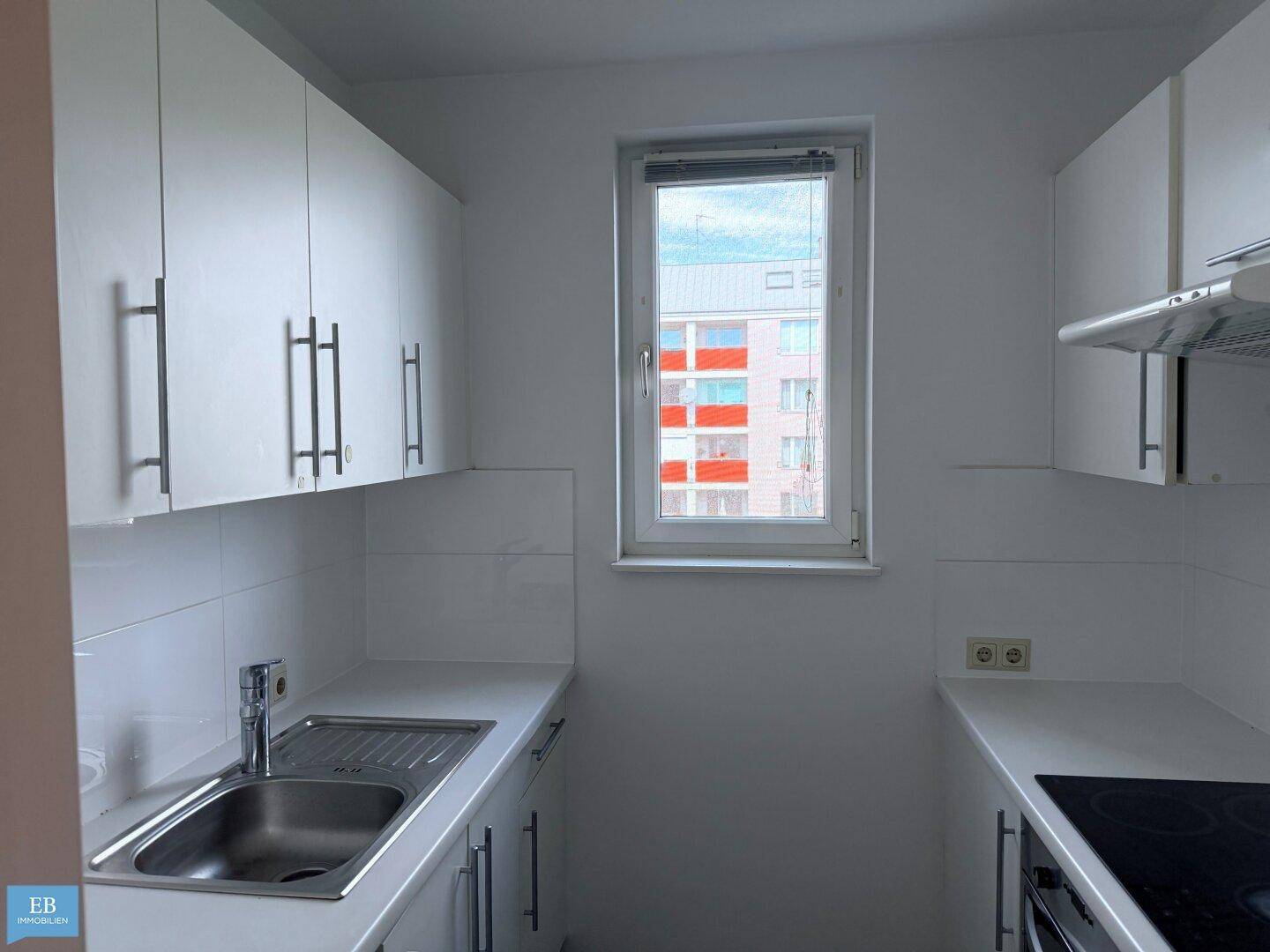 Helle Küche mit weißen Schränken, Spüle und Induktionskochfeld, gut beleuchtet durch ein Fenster.