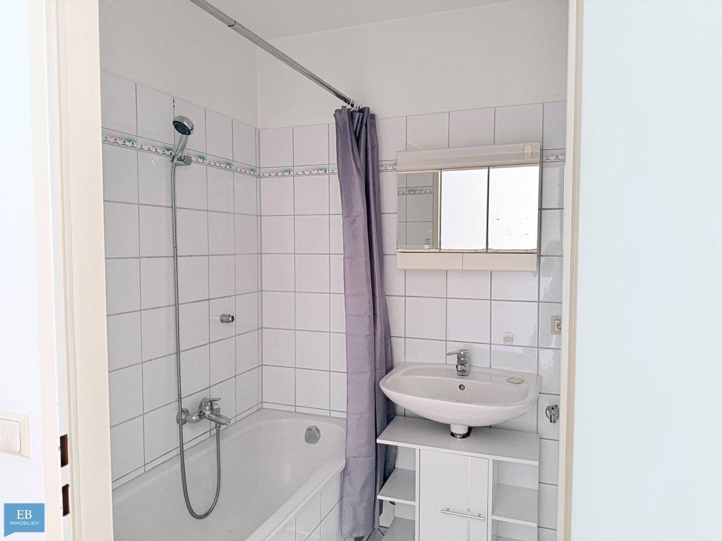 Gefliestes Badezimmer mit Badewanne, Duschvorhang, Waschbecken und Spiegelschrank.