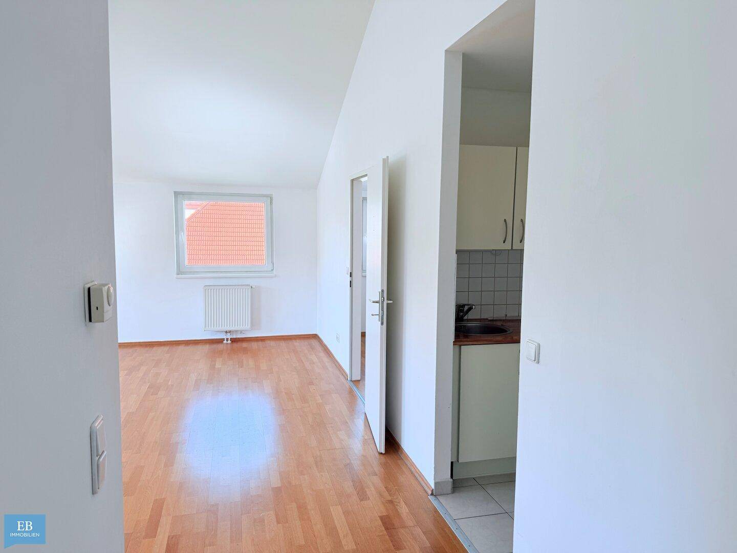 Helles Wohnzimmer mit Holzparkettboden und Blick auf eine kleine, separate Küche.