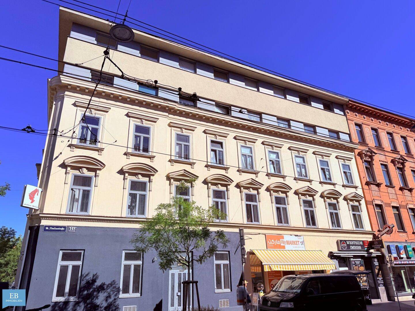 Historisches Gebäude mit moderner Dachaufstockung, Geschäften im Erdgeschoss und Straßenbahnlinien.