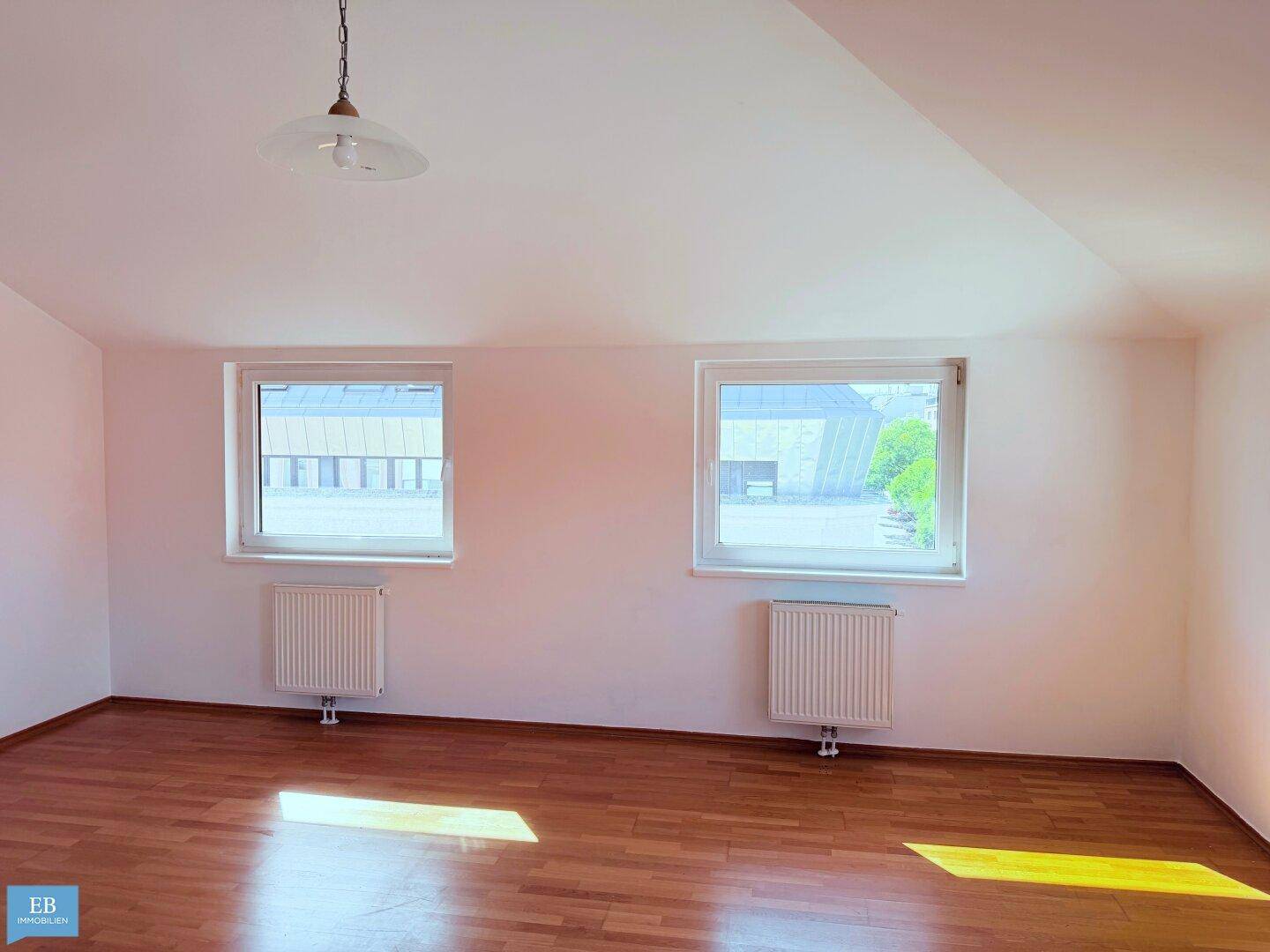 Geräumiges Zimmer mit Holzparkettboden, zwei Fenstern und Heizkörpern, bietet viel Tageslicht und eine helle Atmosphäre.