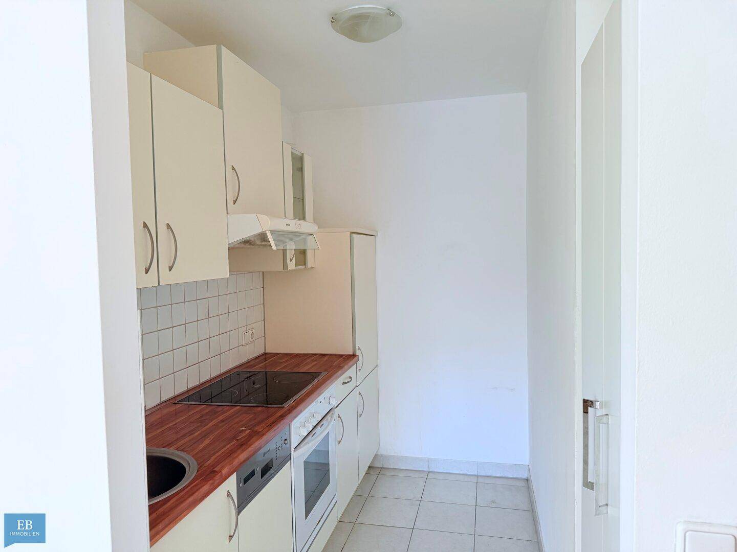 Kleine, funktionale Küche mit hellen Schränken, Holz-Arbeitsplatte und integrierten Geräten.